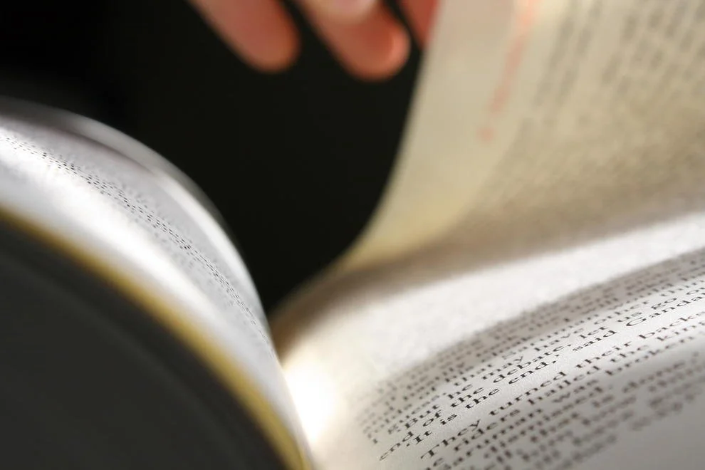 Close-up of a person holding an open book with visible text on the pages.