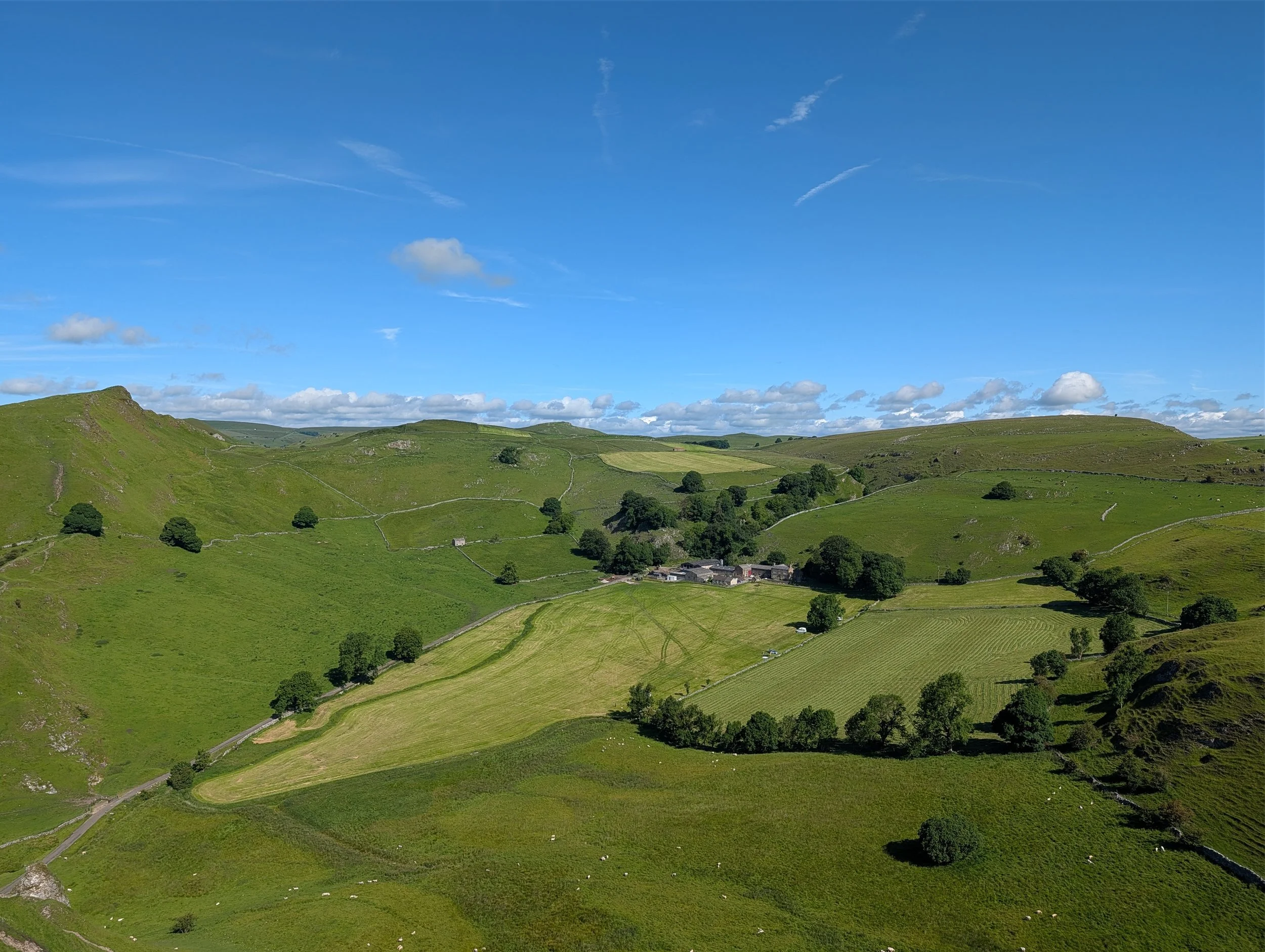 Scenic view of rolling green hills with a clear blue sky and scattered clouds.