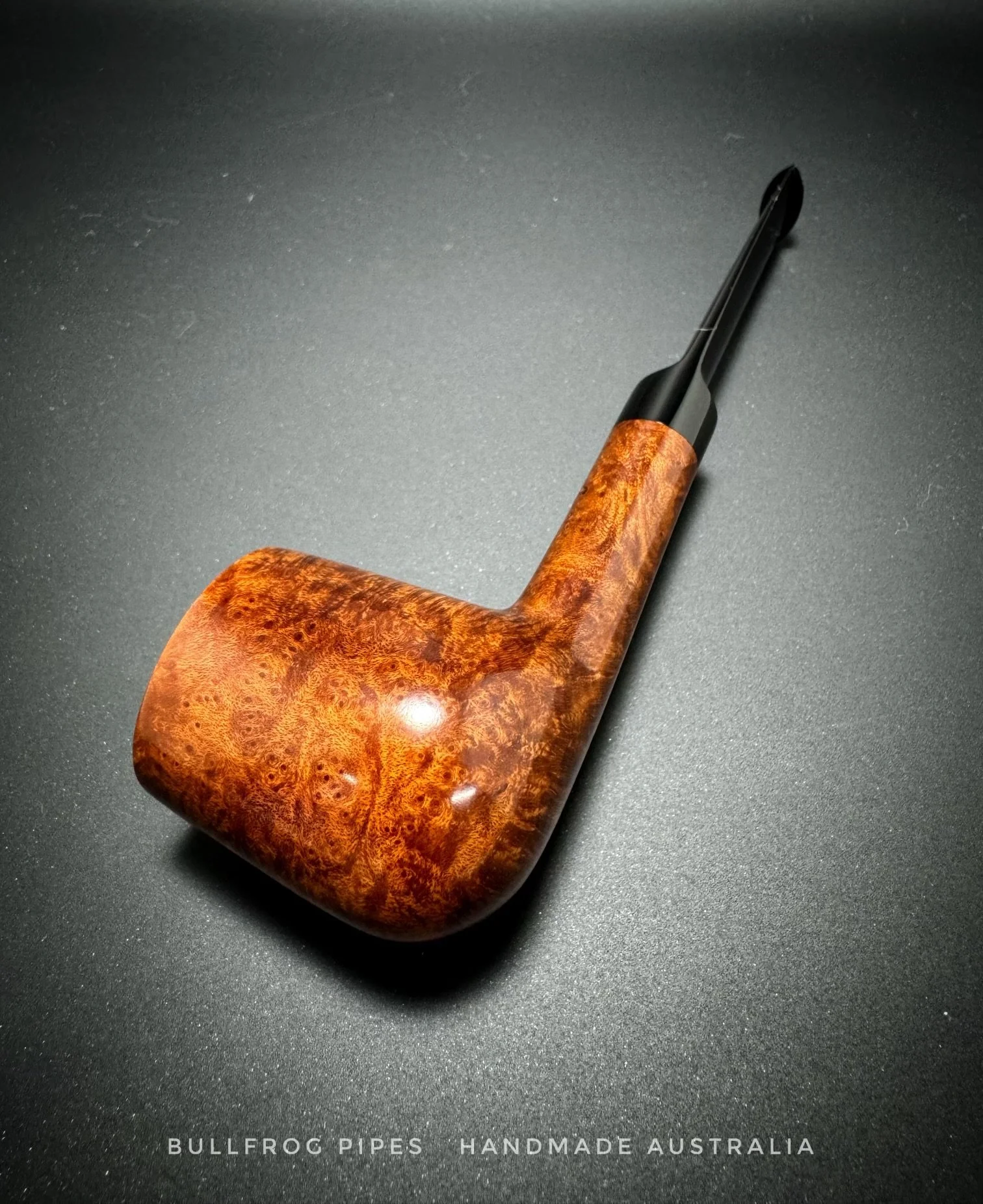 A handcrafted wooden smoking pipe with a curved design placed on a black surface, with text at the bottom that says 'Bullfrog Pipes Handmade Australia'.