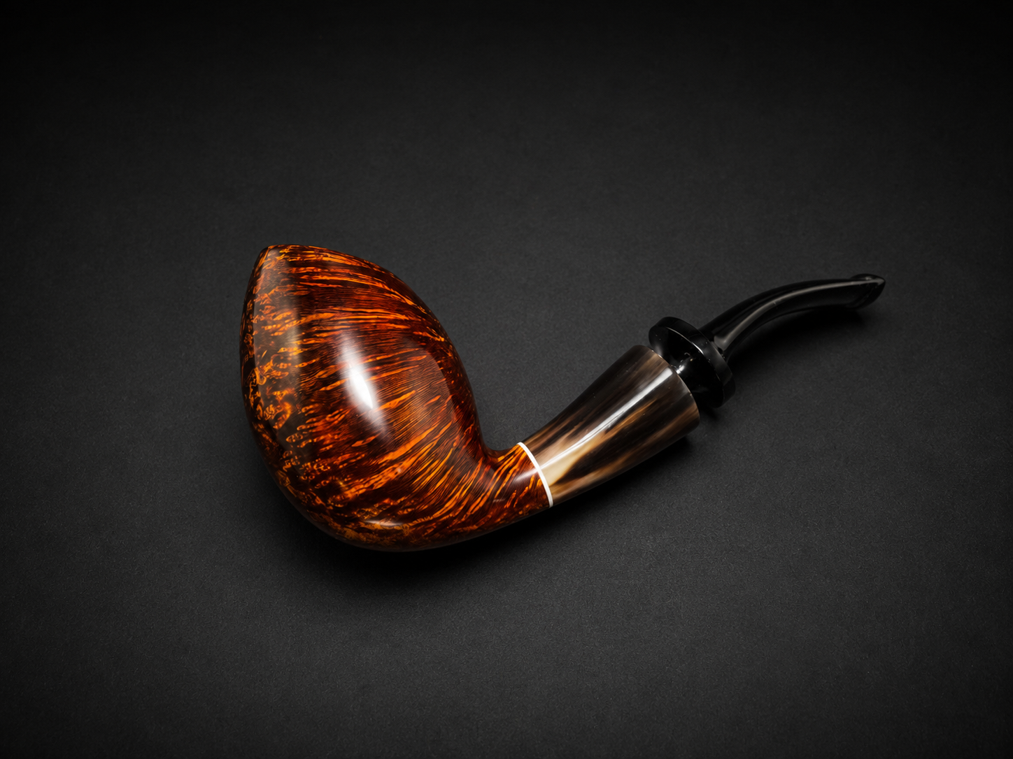 A close-up of a smoking pipe with a brown and black speckled bowl and a black curved stem, placed on a black surface.