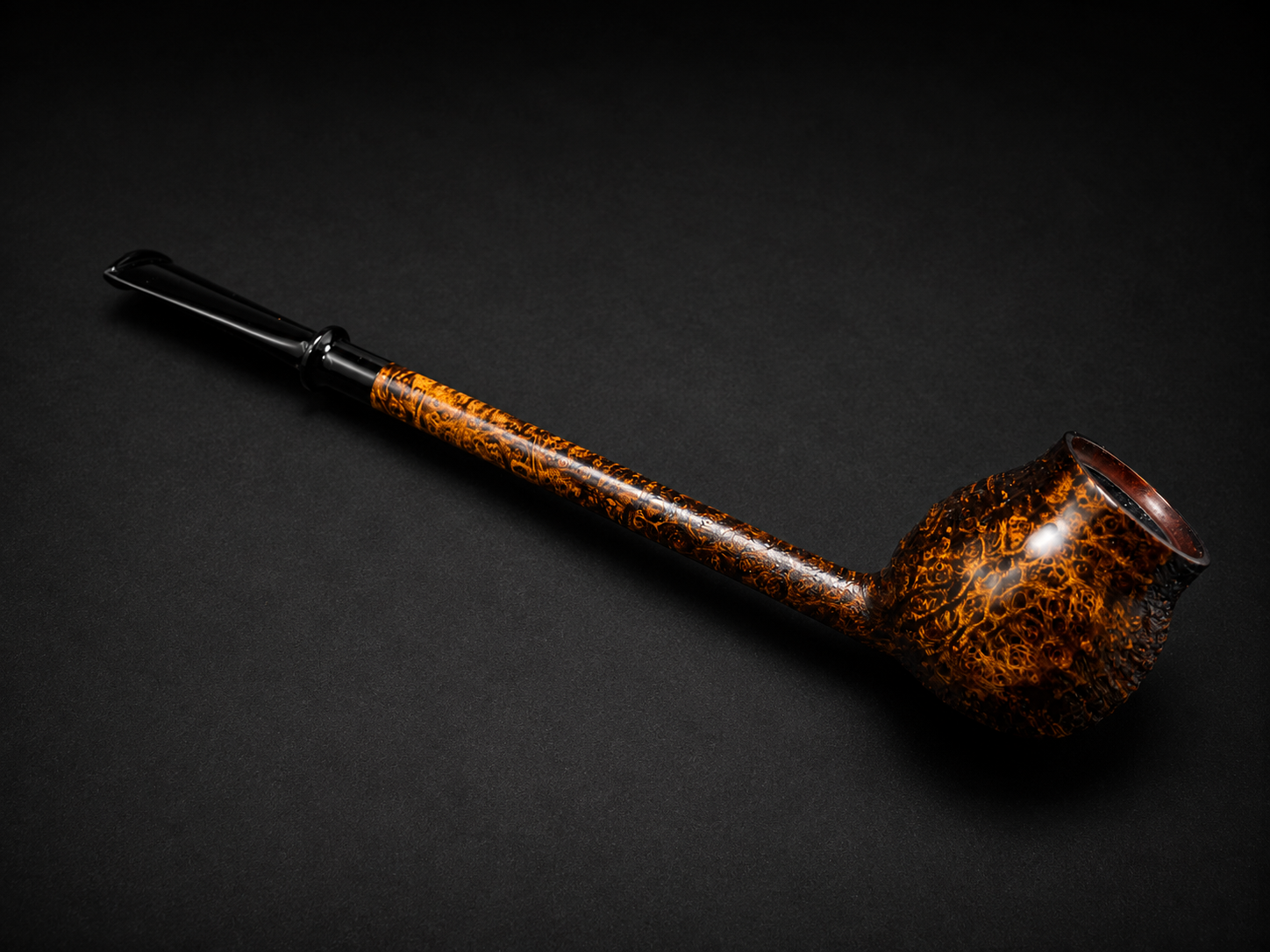 A smoking pipe with a ornate, orange and black patterned bowl and stem, placed on a black background.