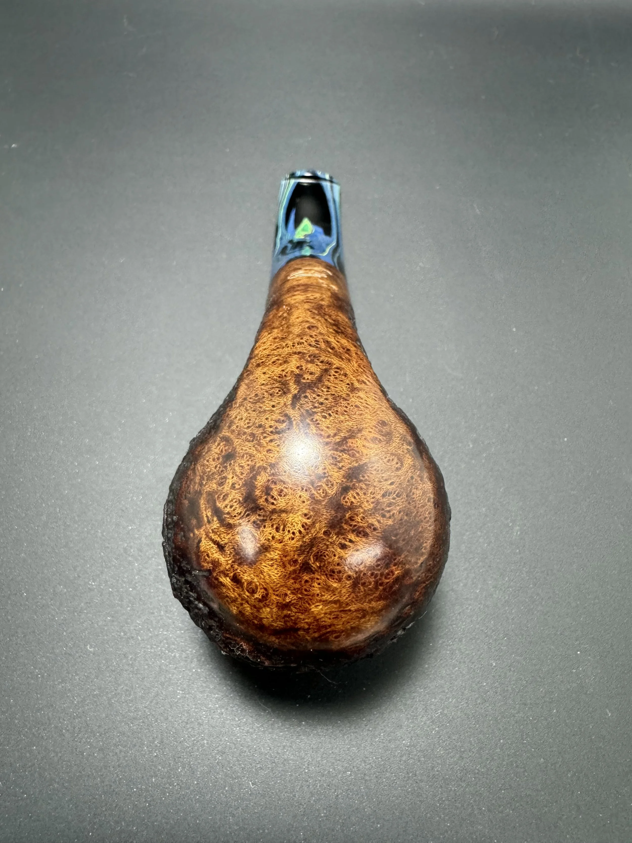 A polished, highly reflective metal tool with a textured, wooden handle, seen from the top down on a dark gray surface.