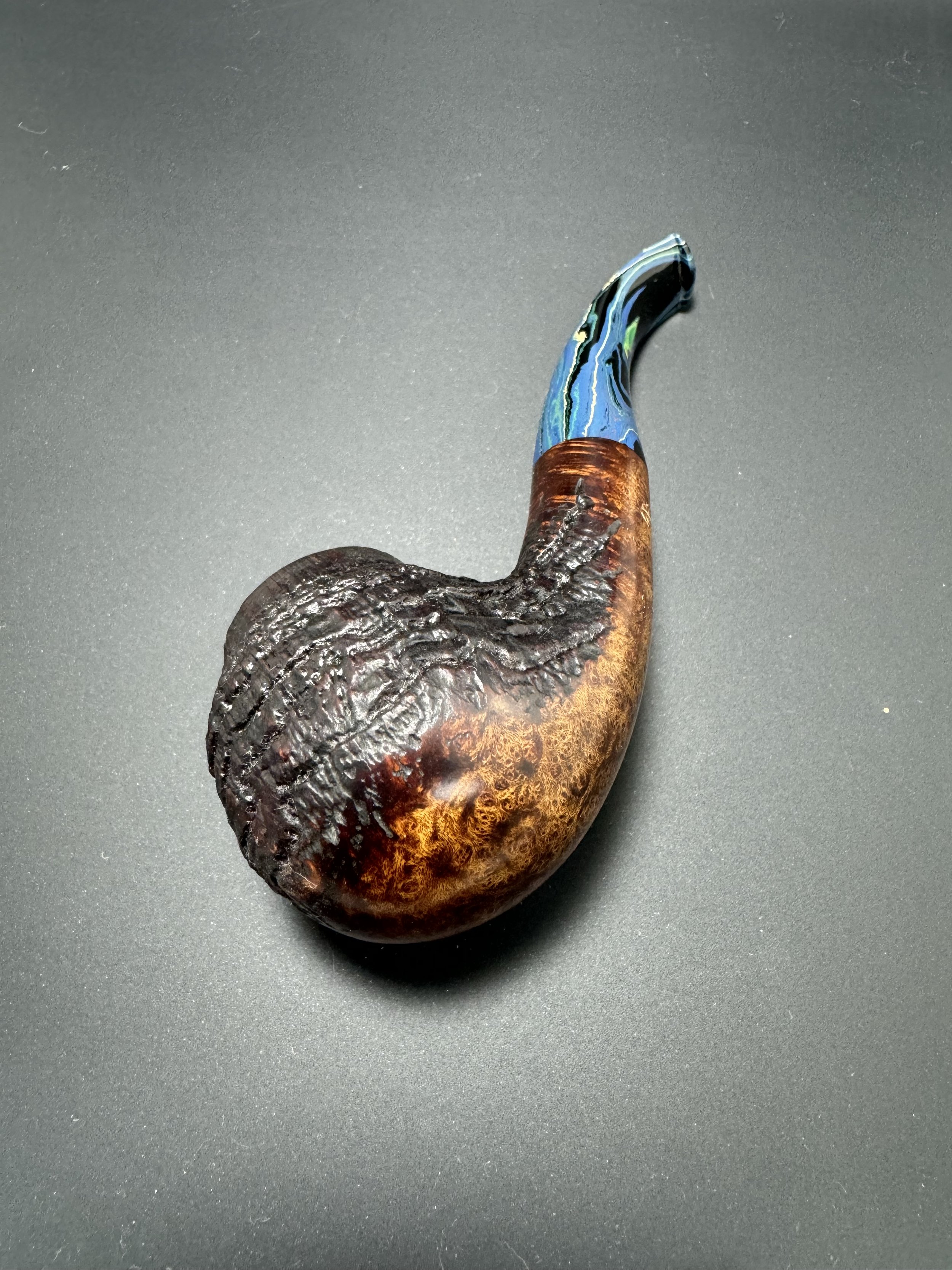 A unique pipe with a textured brown base and a colorful, swirled glass stem on a black surface.
