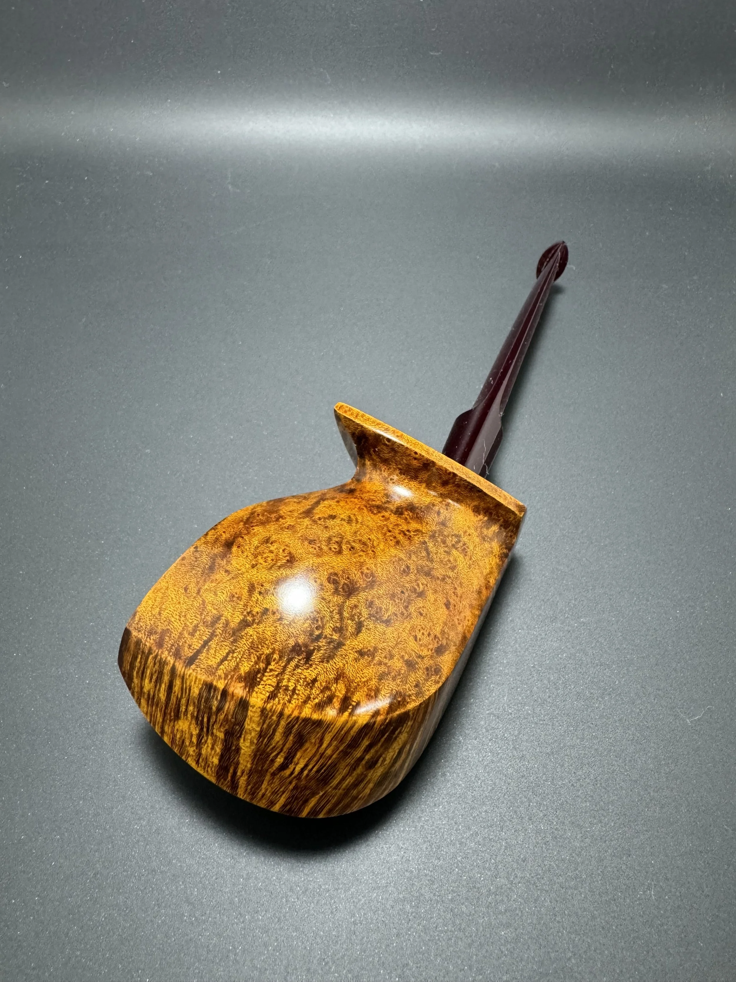 A wooden spoon with a rounded, shiny bowl and a dark handle, resting on a black surface.