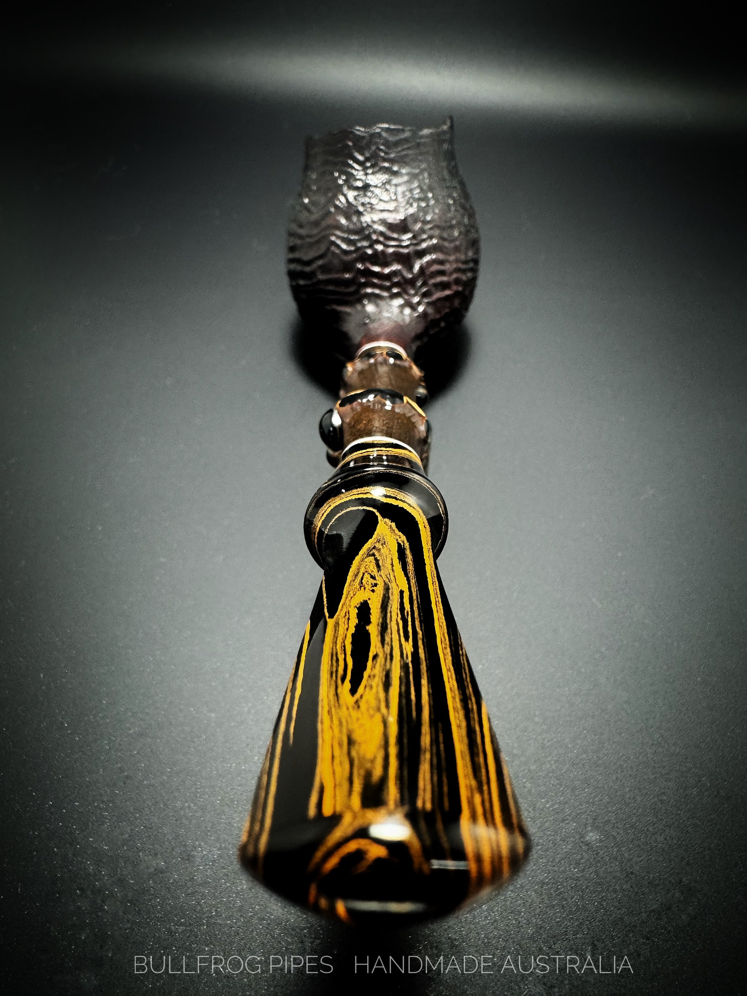 A handcrafted bowl with water ripples on its surface, placed on a dark background with a black and yellow patterned pipe behind it.