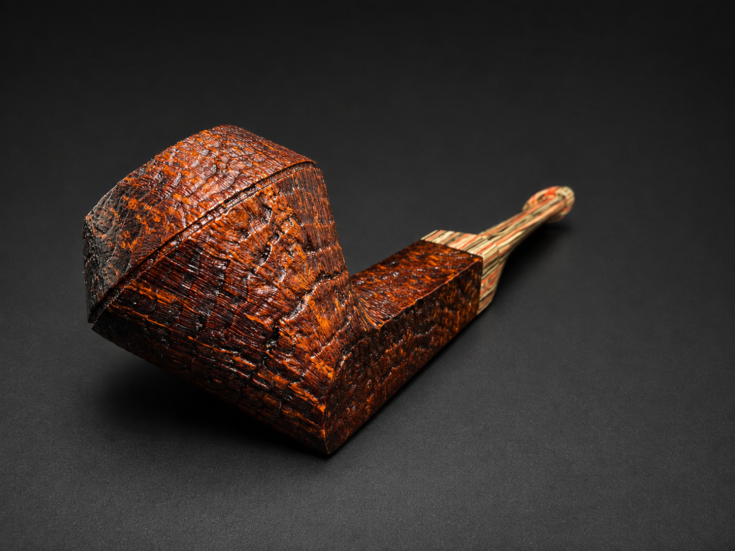 A decorative smoking pipe with a textured, reddish-brown bowl and a multi-colored striped stem, placed on a black background.