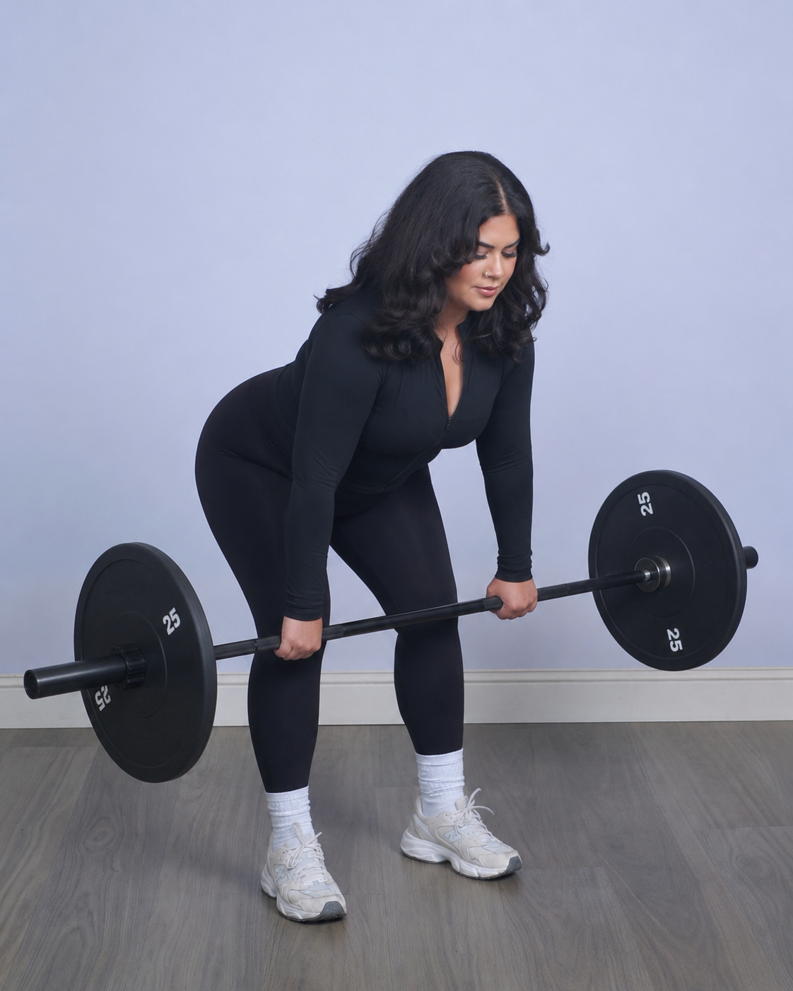 Woman in black workout clothes lifting a barbell with weights in a gym.