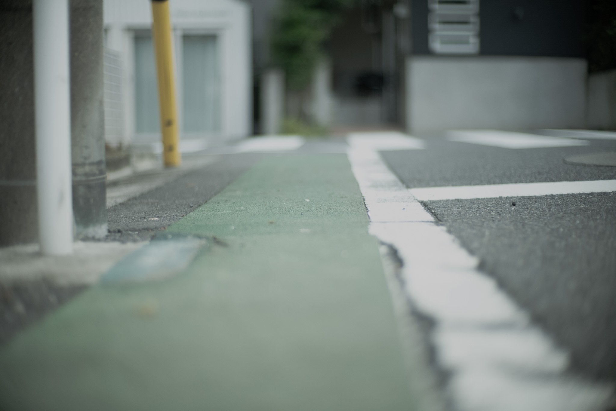 街の歩道で白線と緑色のラインが引かれた自転車レーン。左右にポールが立っている。