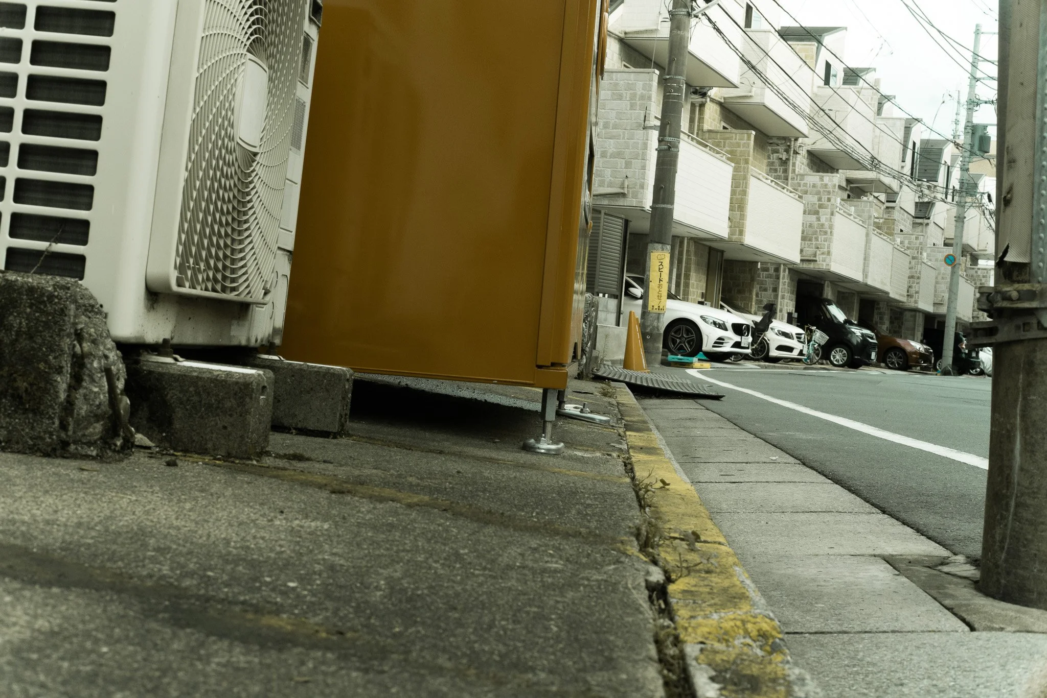 アパートメントの駐車場エリアの路地と路上駐車された車両、電柱と電線。