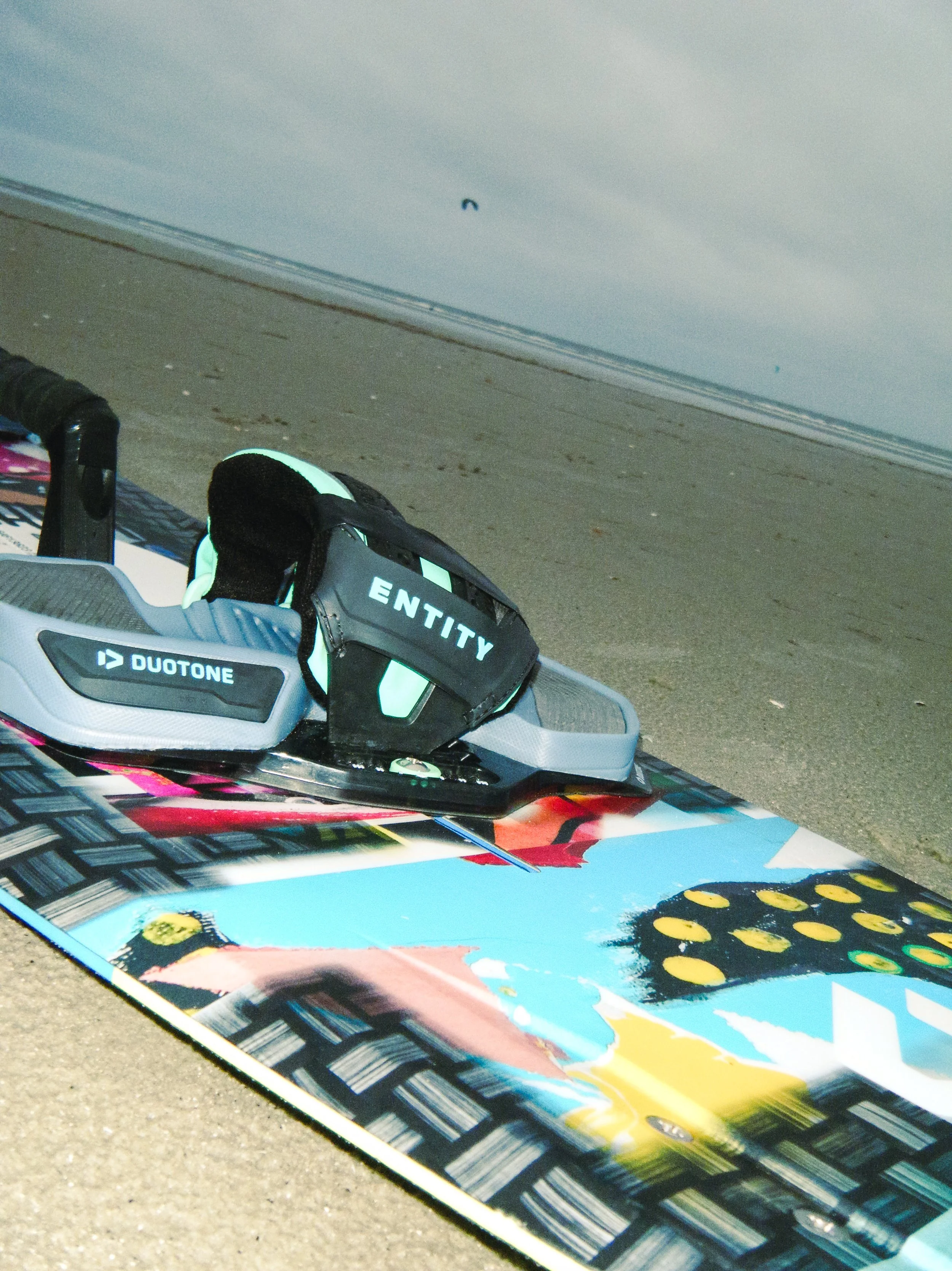 Kiteboard liegt auf dem Boden, im Hintergrund ein Strand.