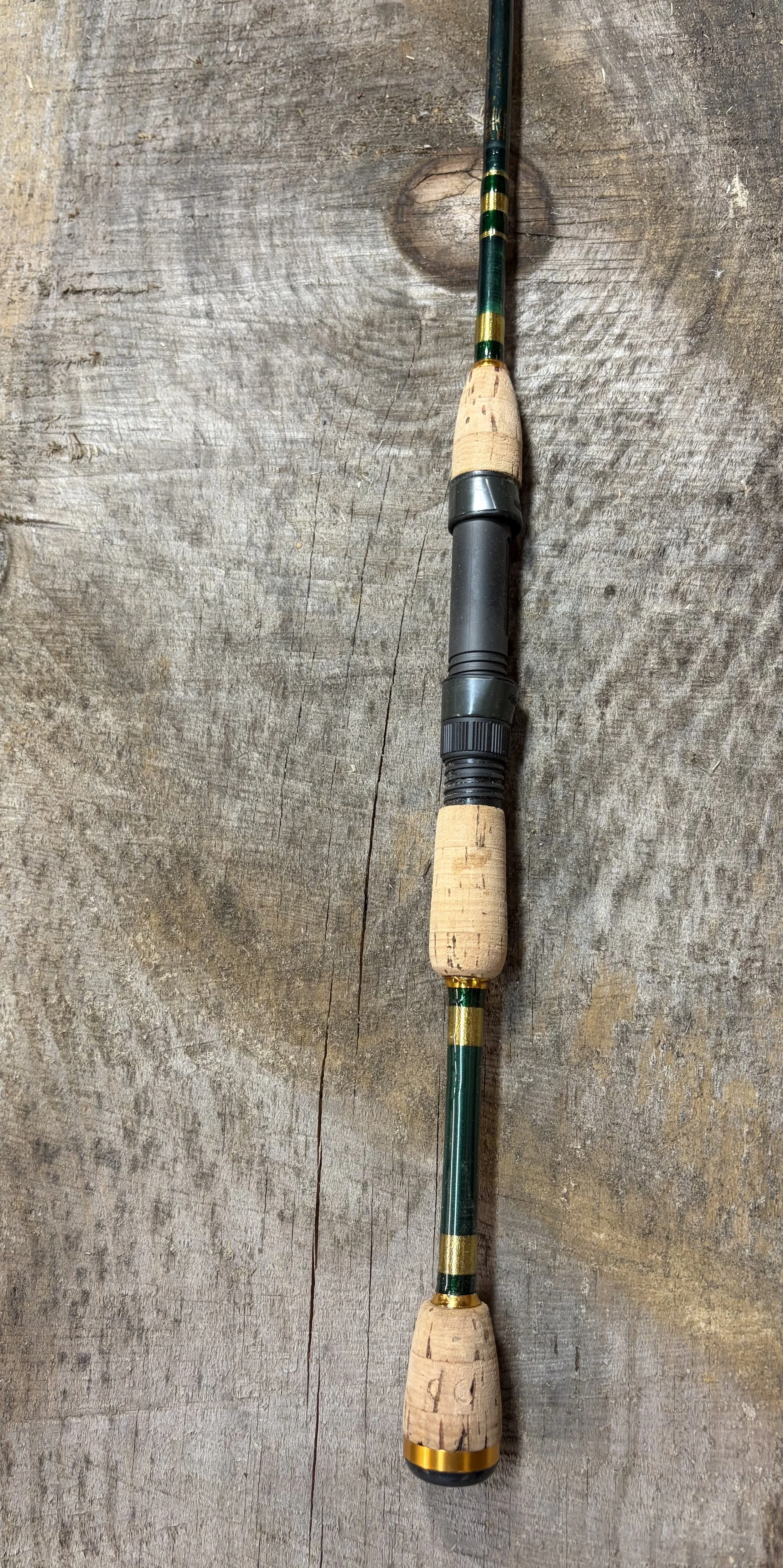 A fishing rod with cork handles and a green and yellow striped rod, lying on a rustic wooden surface.