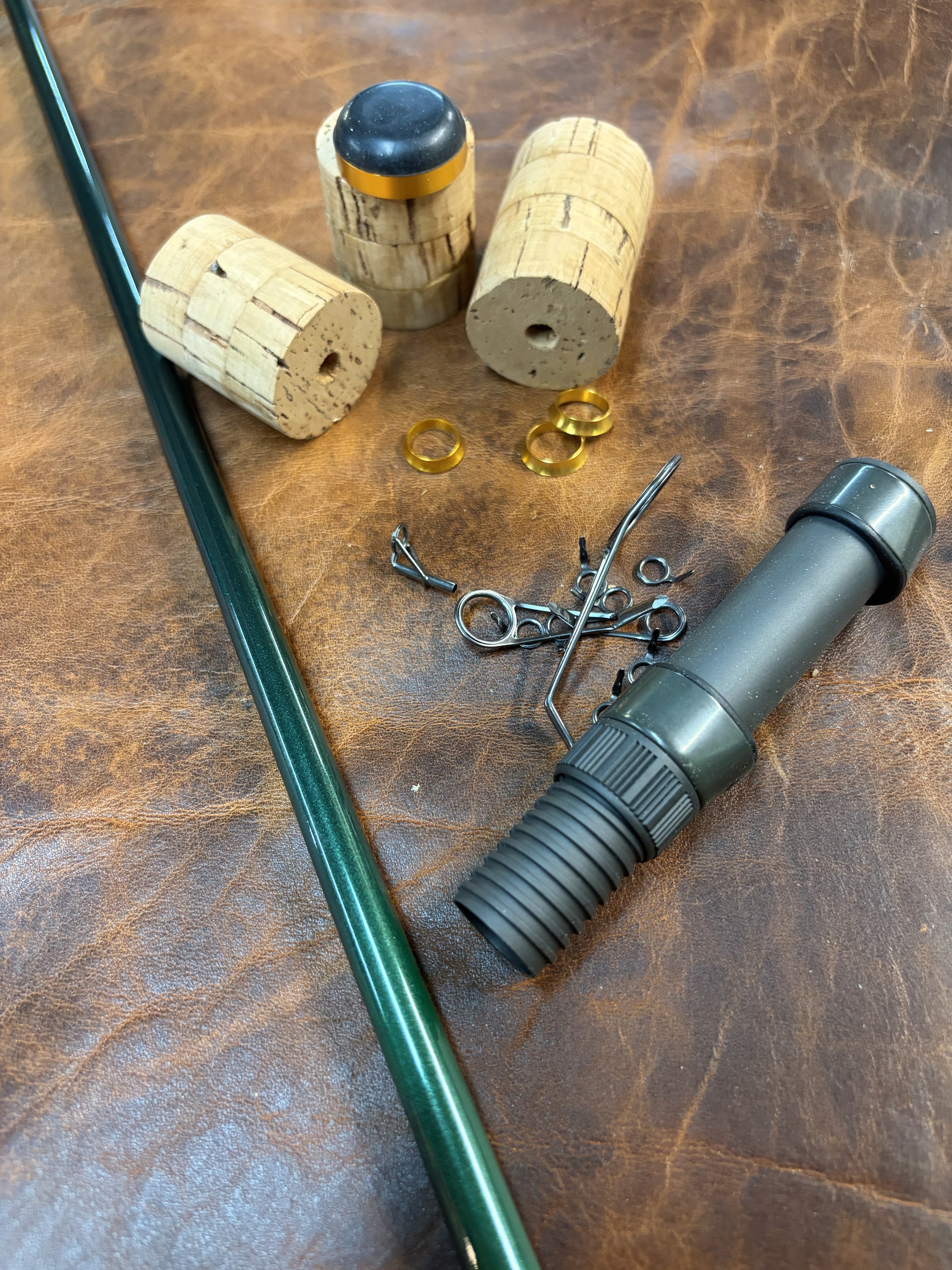 A collection of rod parts including  cork, a green blank, a graphite reel seat, and guides on a wooden surface.