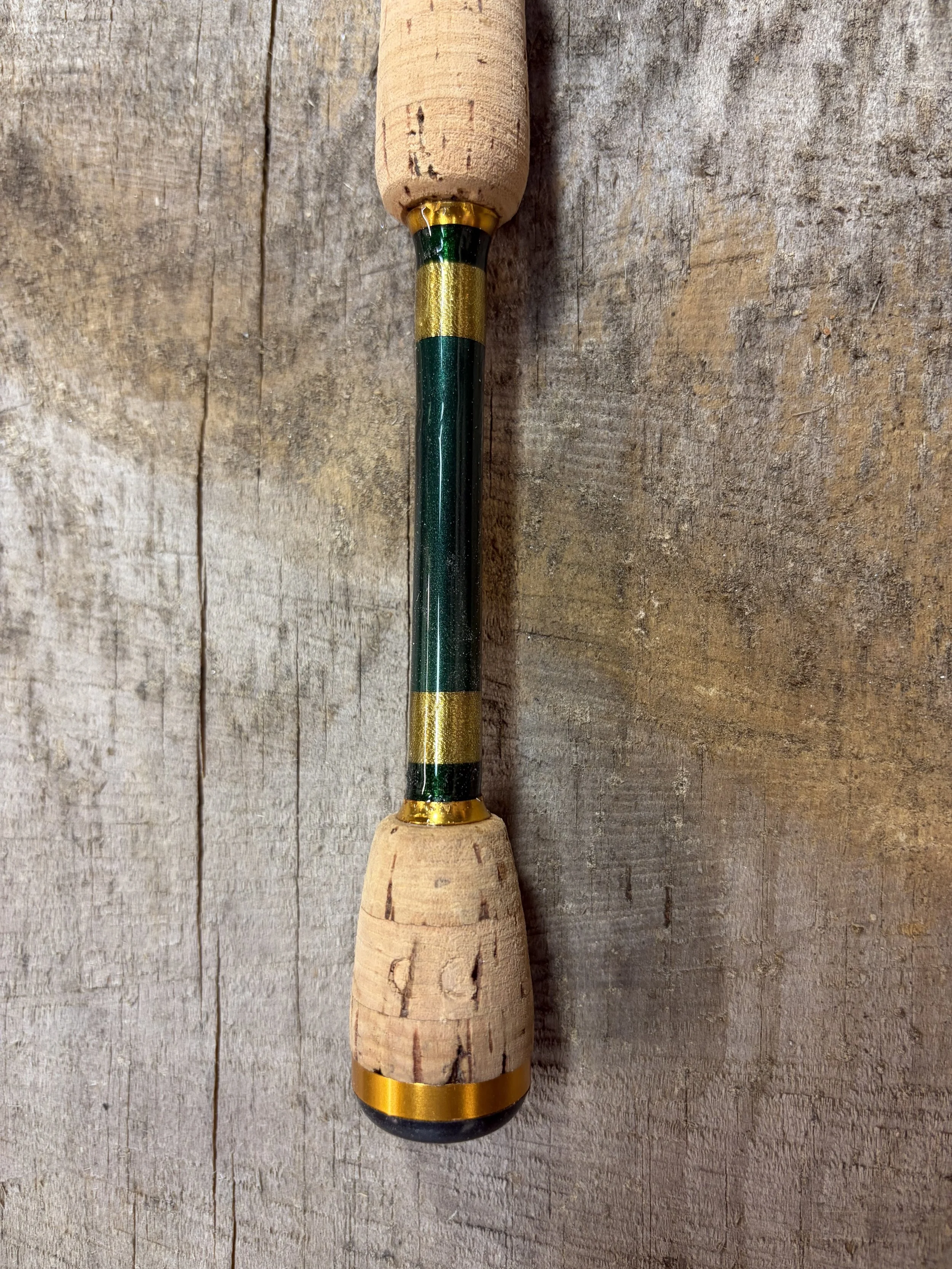 Fishing rod with a cork handle and green and yellow accents lying on a wooden surface.