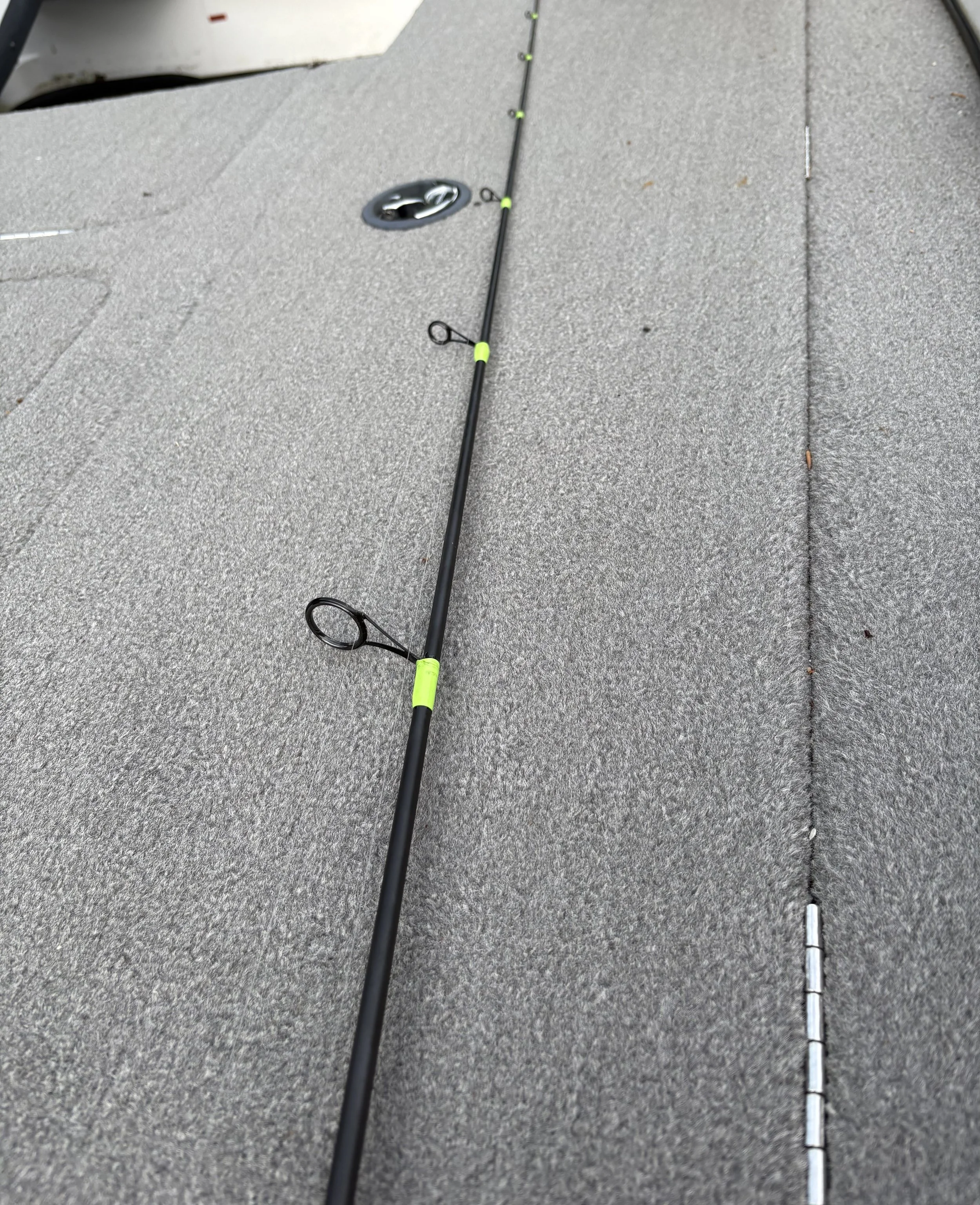 A fishing rod with multiple eyelets lying on the deck of a bass boat.