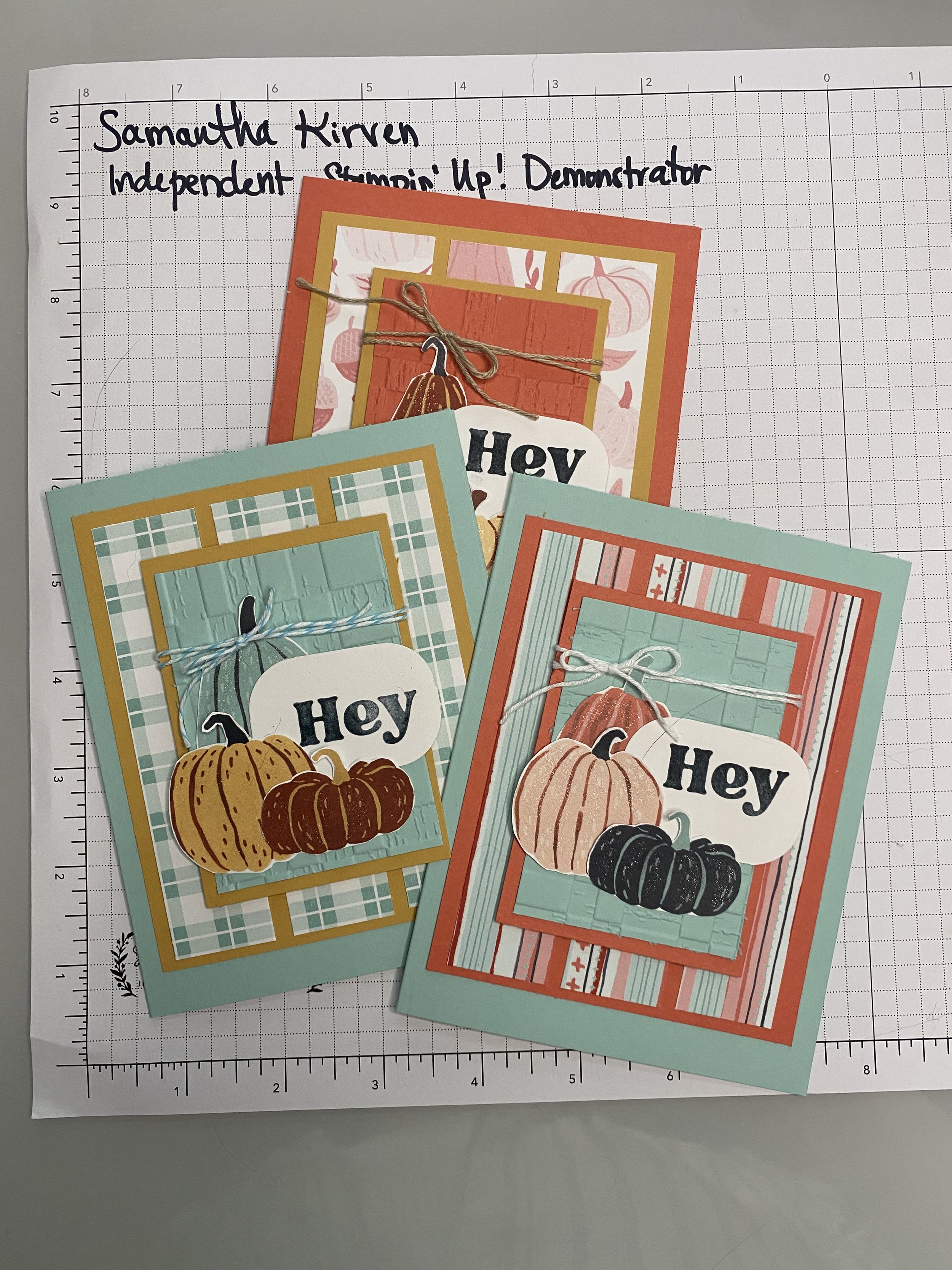 Colorful greeting cards with pumpkin illustrations and the word 'Hey' on a grid cutting mat.