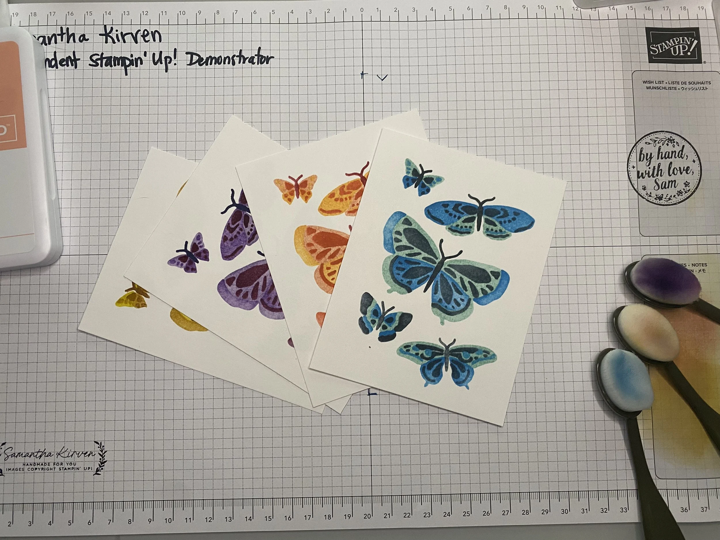 Colorful butterfly stickers on white paper, scissors, ink pad, and a grid cutting mat with a ruler.