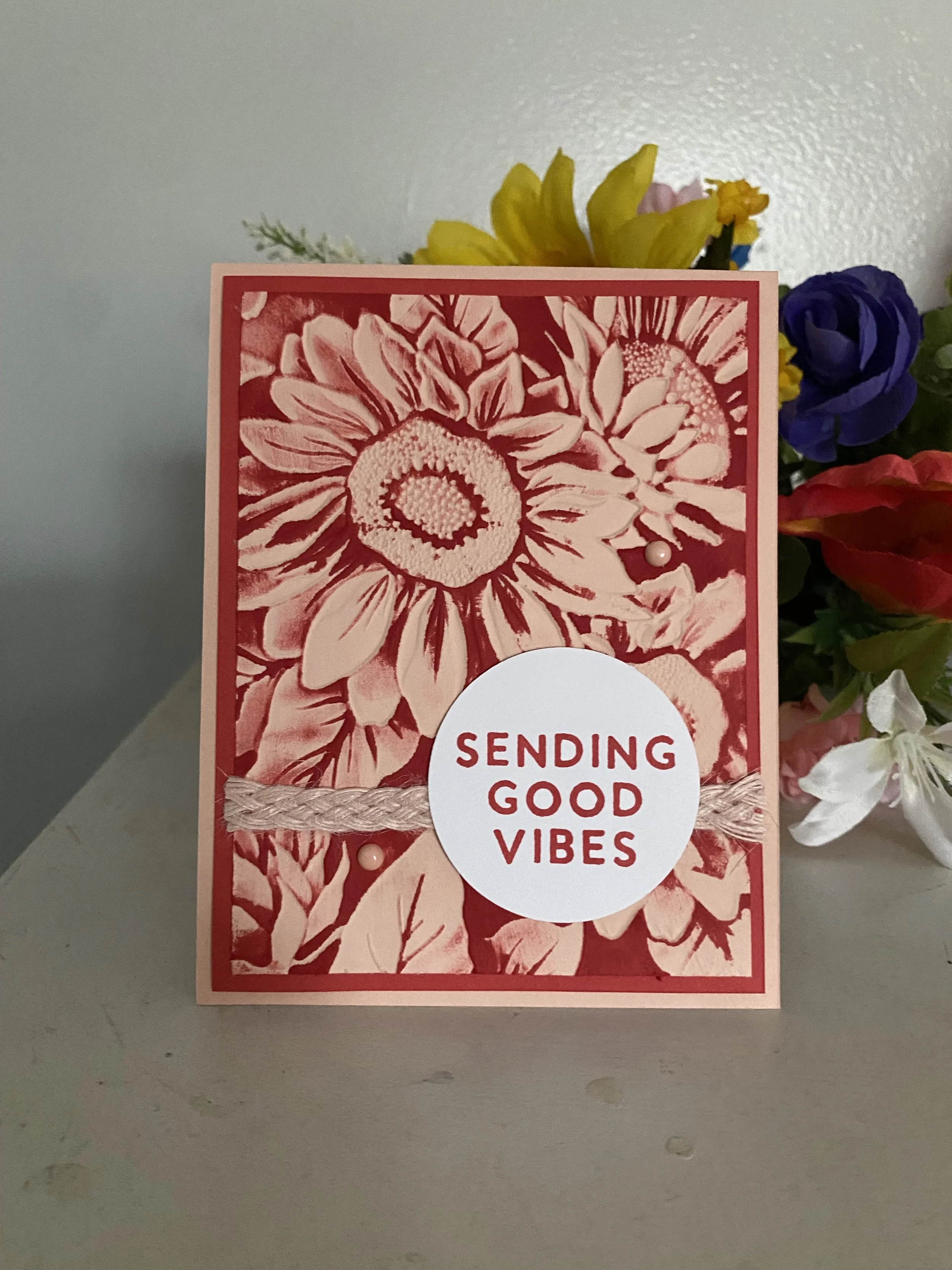 A greeting card placed in front of a bouquet of colorful flowers contains the message 'Sending Good Vibes.'