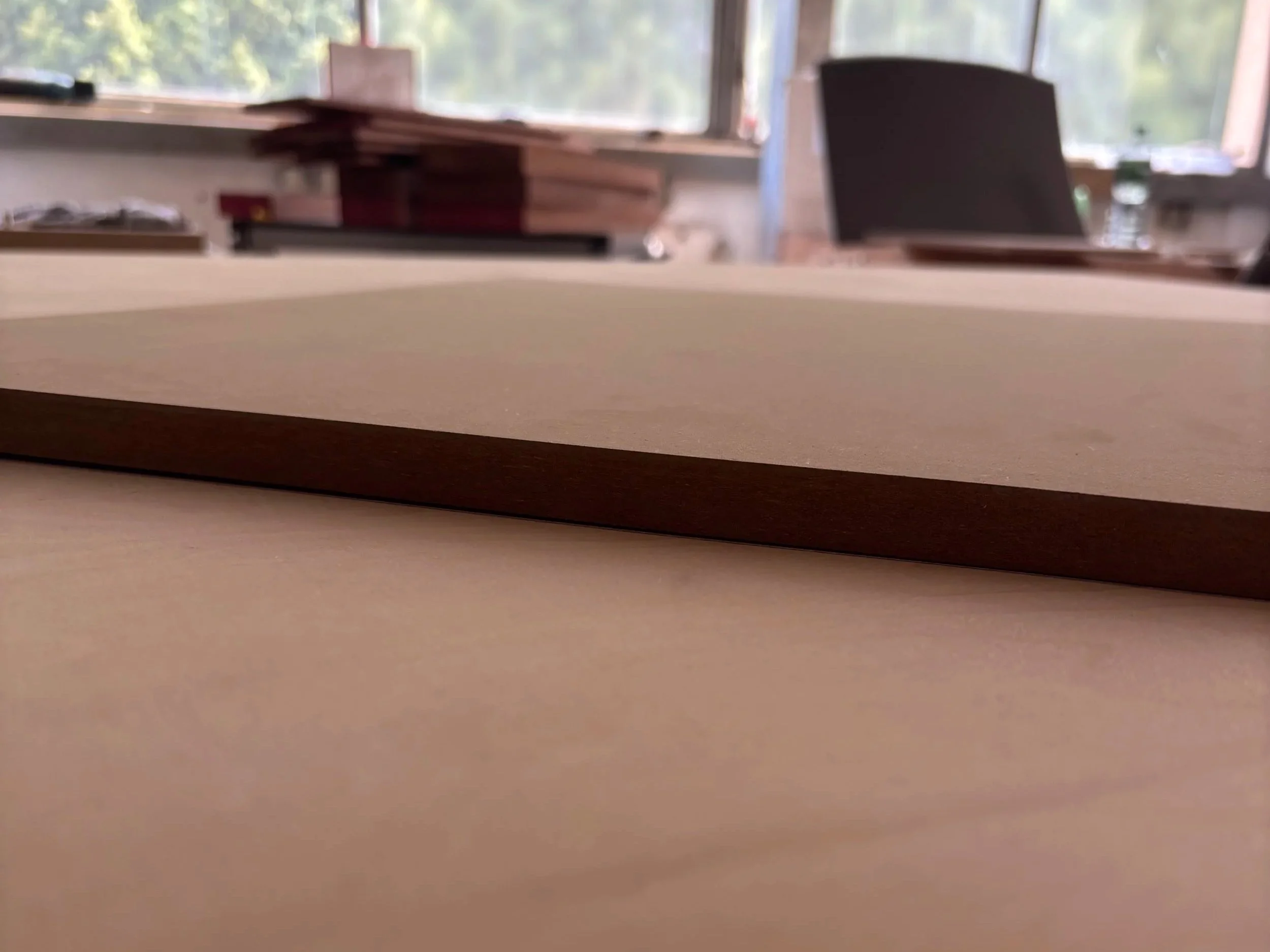 Büro mit Schreibtischen, Stühlen, Regalen und großen Fenstern, durch die Tageslicht scheint.