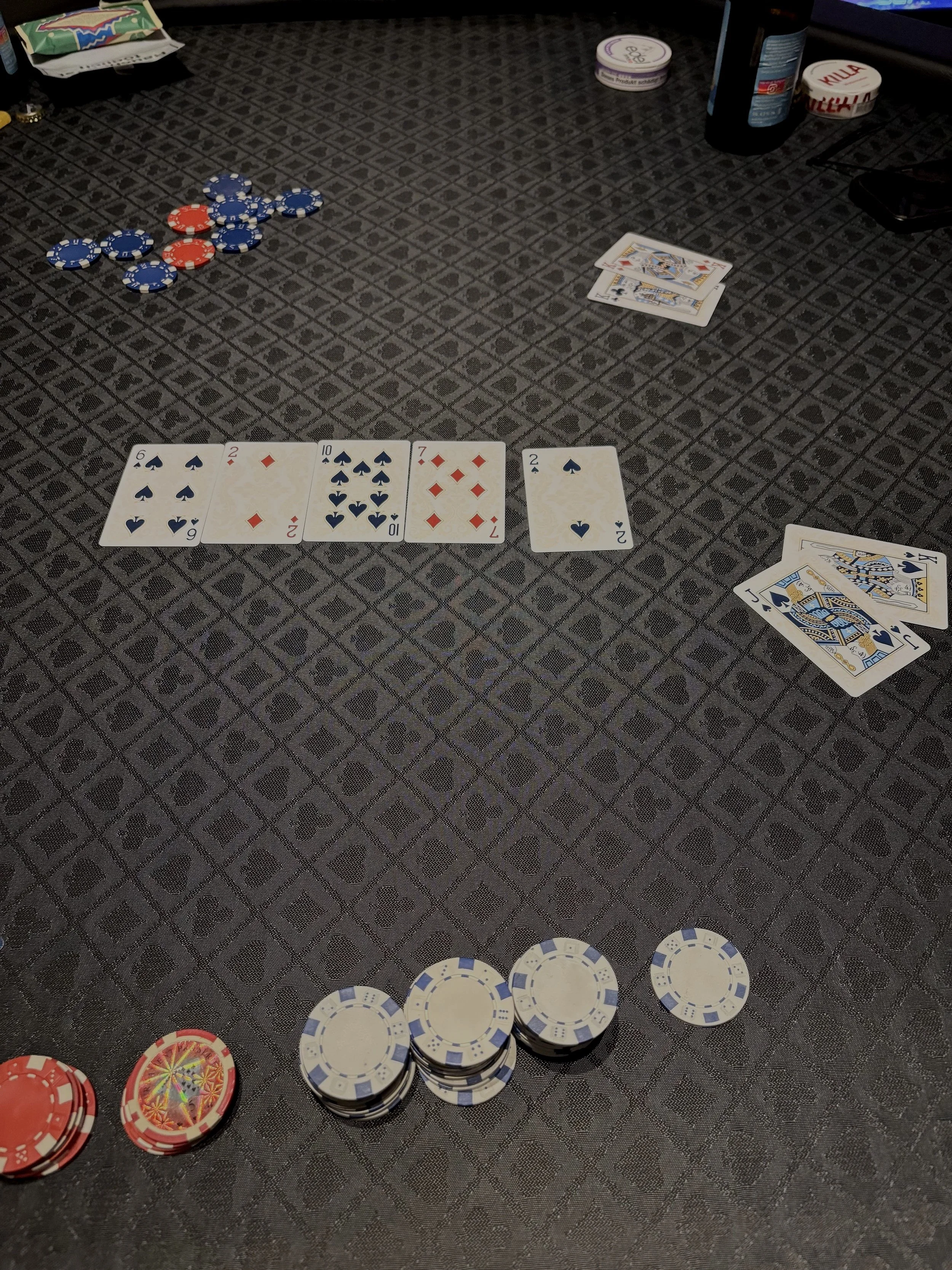 Auf einem Spieltisch liegen Pokerkarten, Chips und Getränke, vermutlich bei einem Poker- oder Casinospiel.
