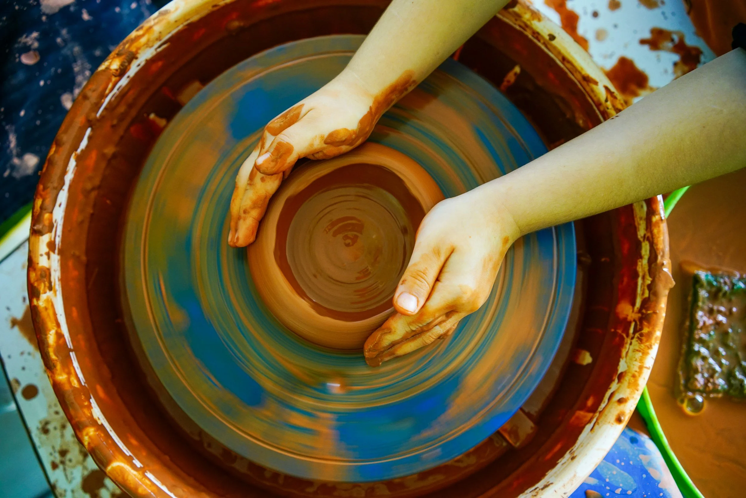 Child shaping clay on a pottery wheel.
