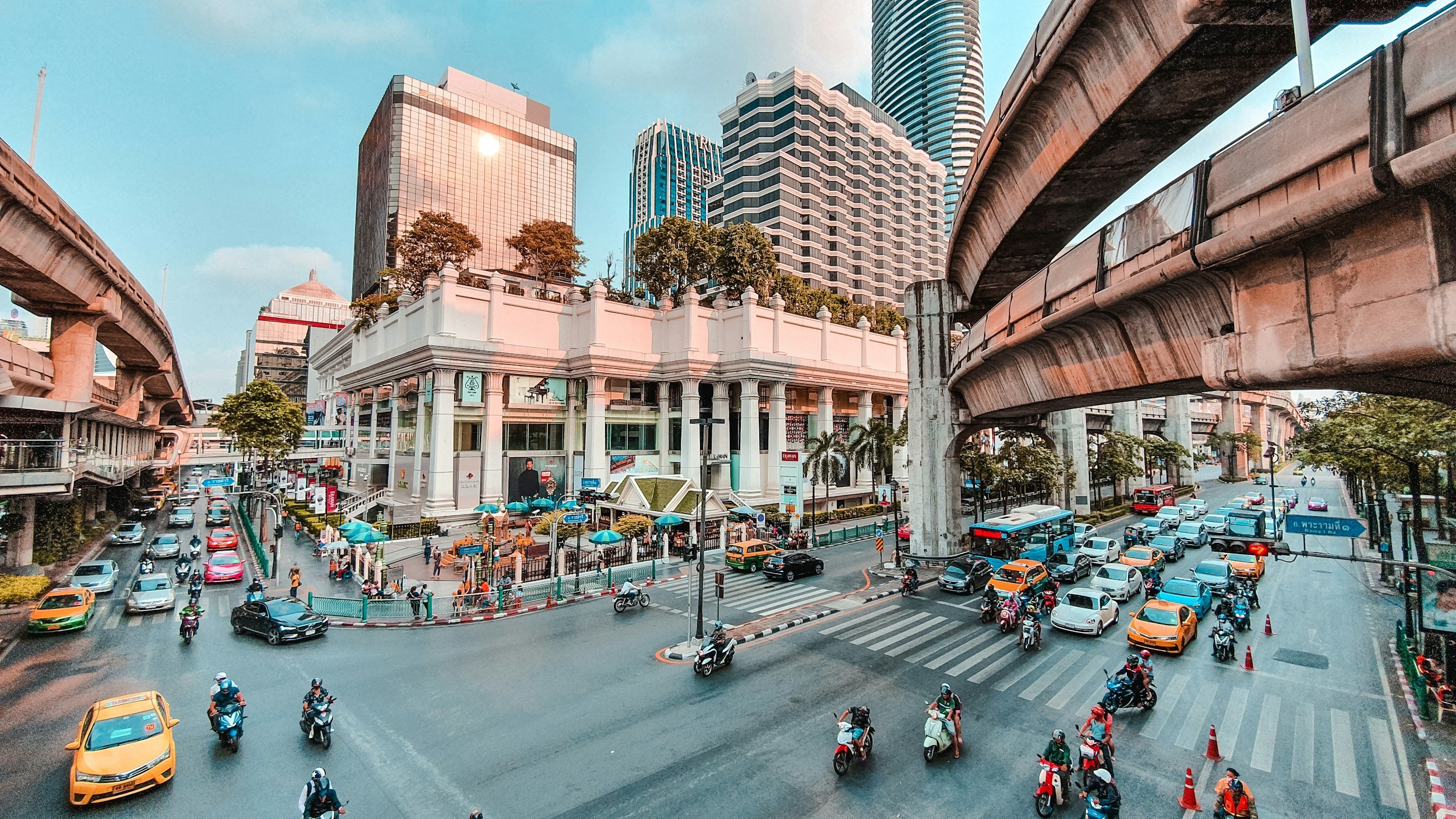 Bangkok city centre with traffic and a Skytrain passing above the street.