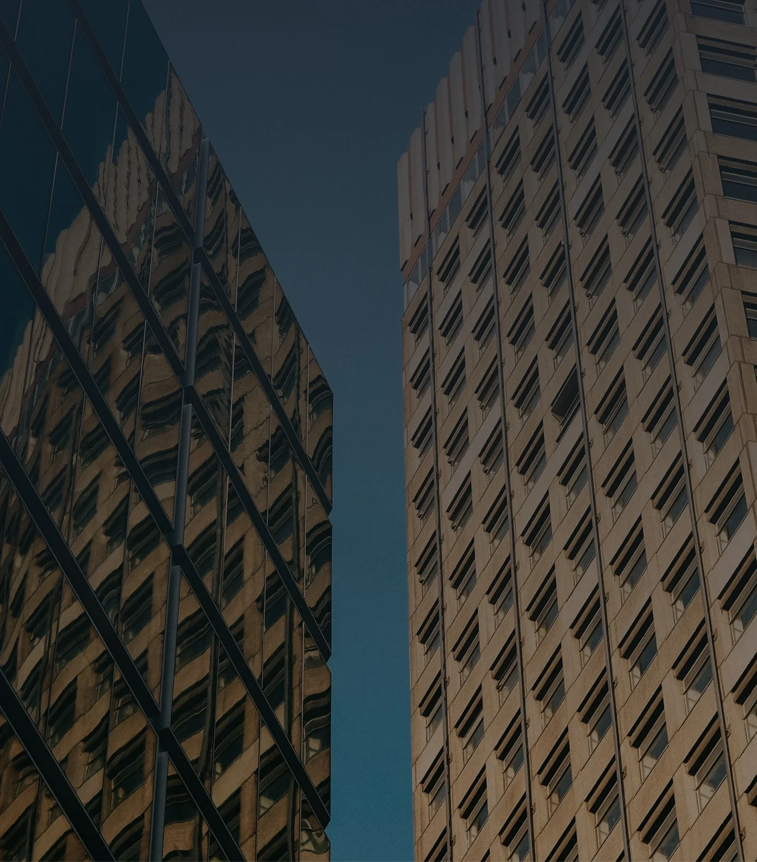 Two tall buildings with glass windows, one with a modern architectural design and the other with a traditional concrete facade, against a clear blue sky.