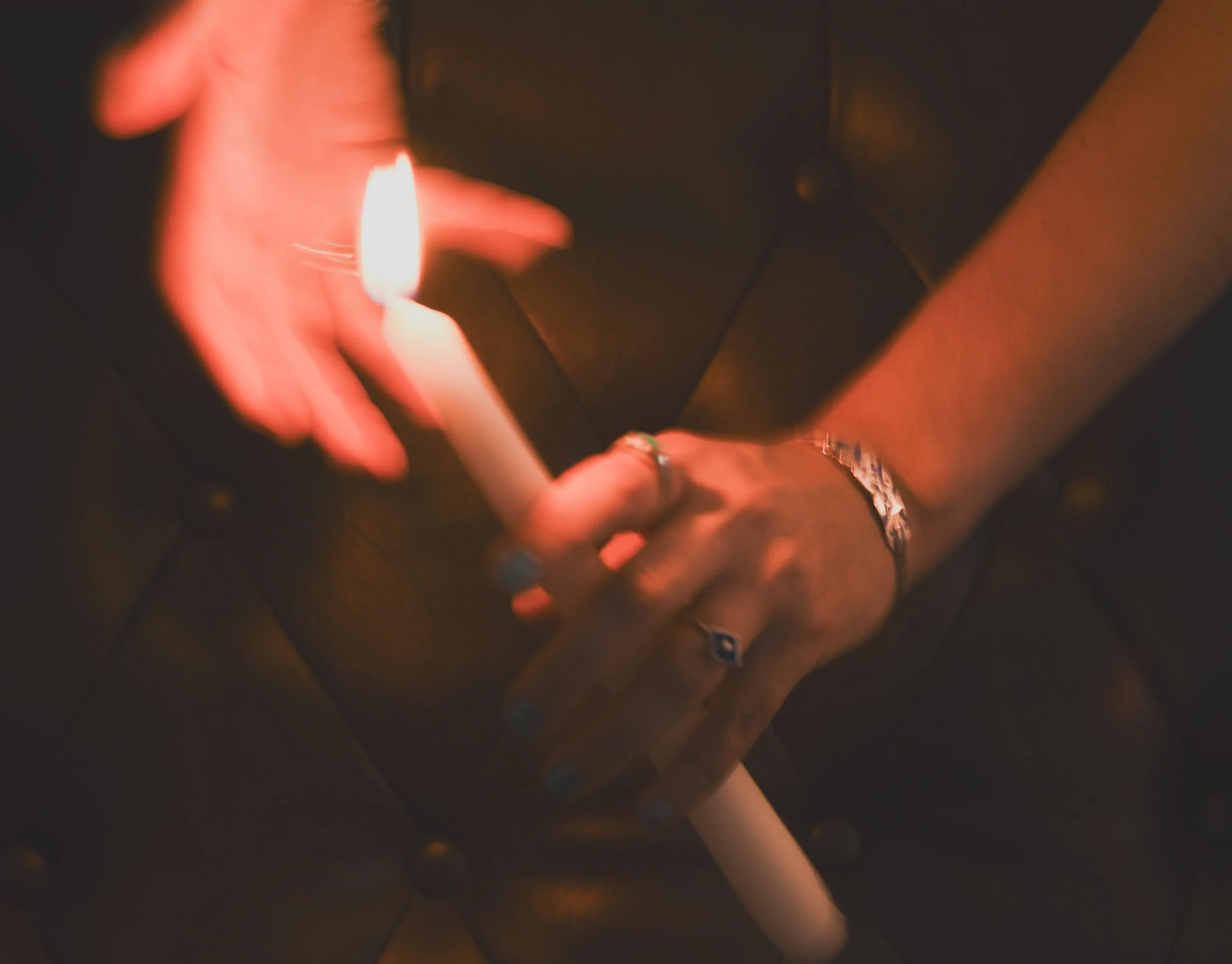 Close-up of a person's hand holding a lit matchstick. The background is dark and the matchstick flame illuminates the fingers.