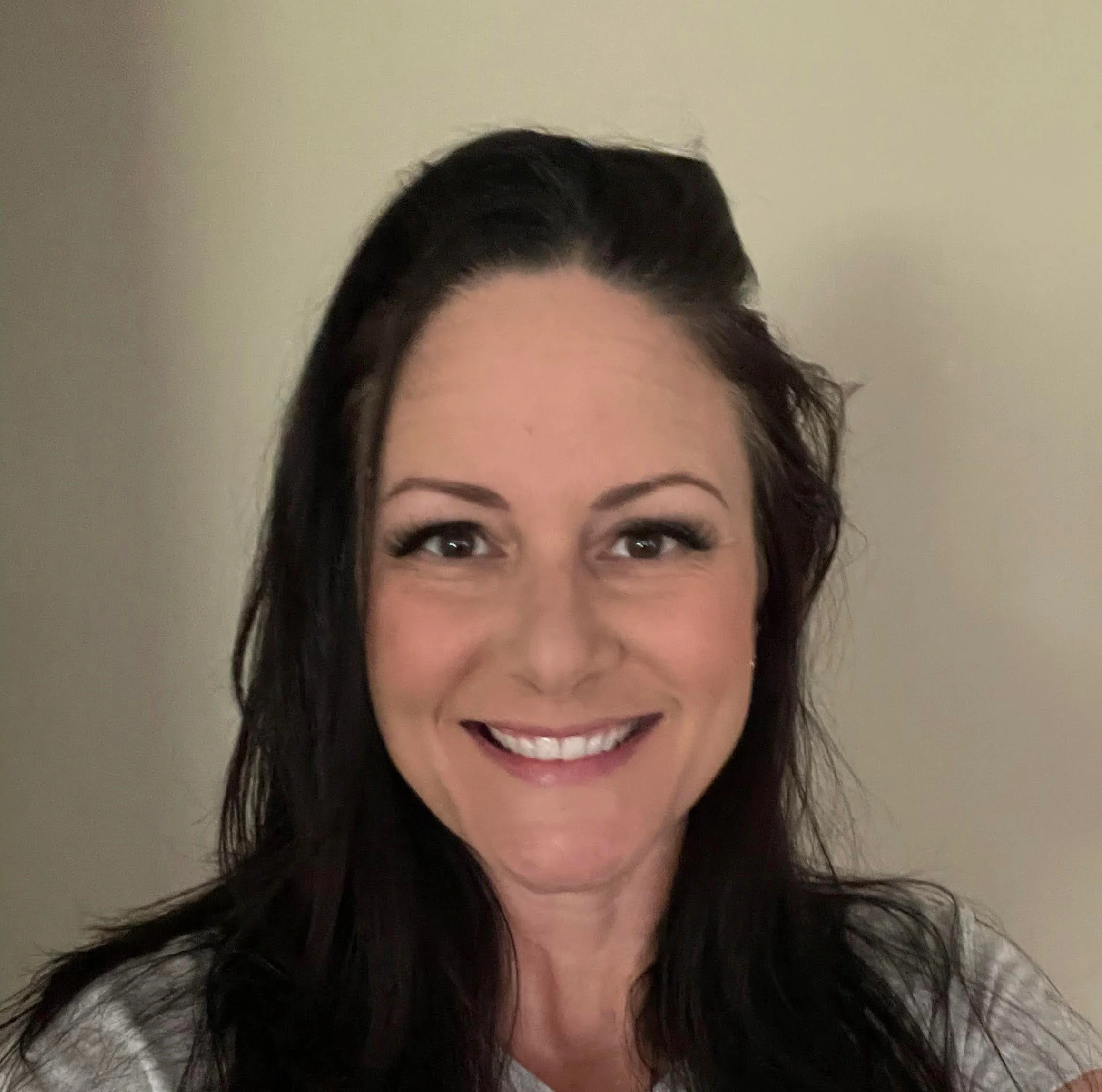 Close-up of a smiling woman with dark hair against a plain background.