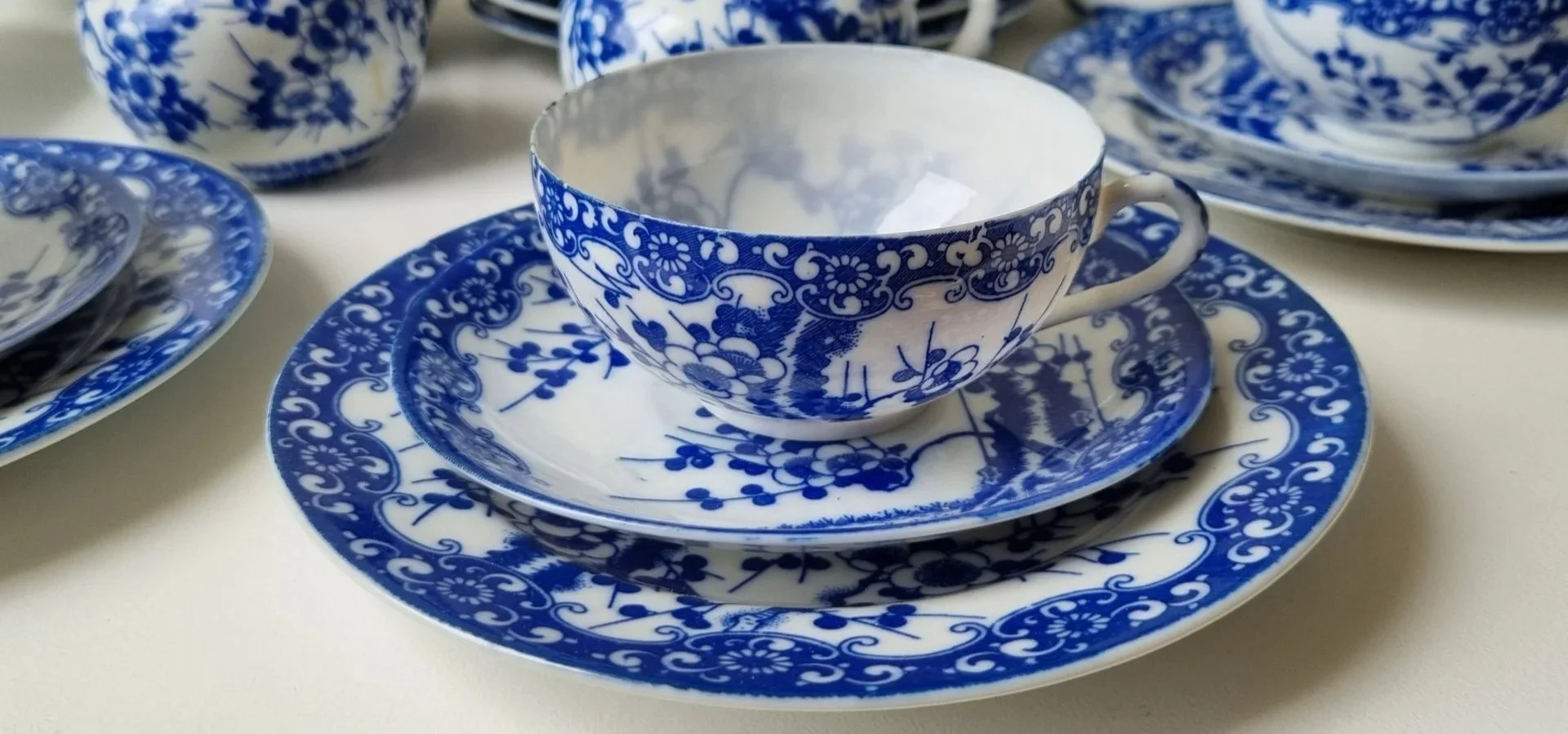 Set di tazze e piatti in porcellana bianca e blu con motivi floreali e grafici, disposti su una superficie chiara.