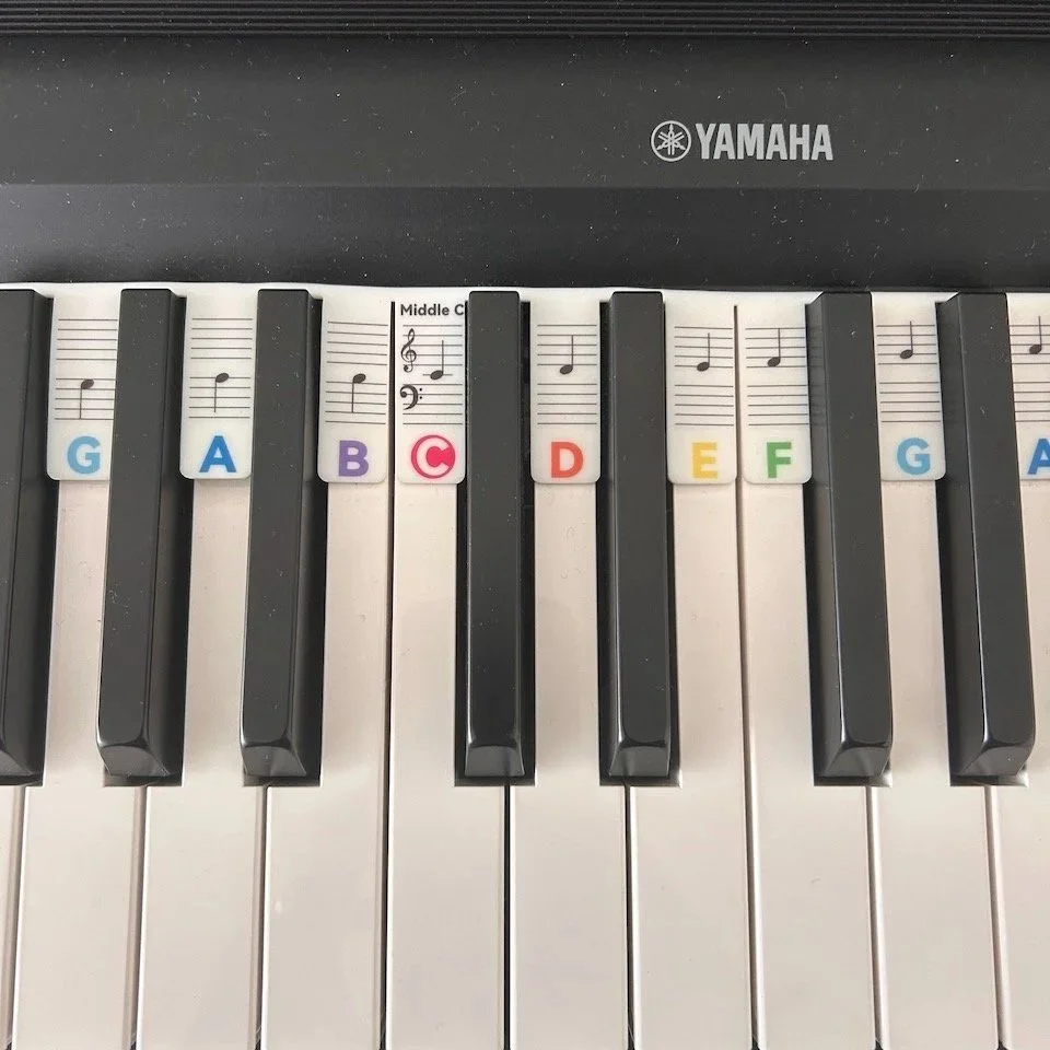 Close-up of a Yamaha keyboard with labeled keys: G, A, B, C, D, E, F, G, A, with colored stickers on the keys.