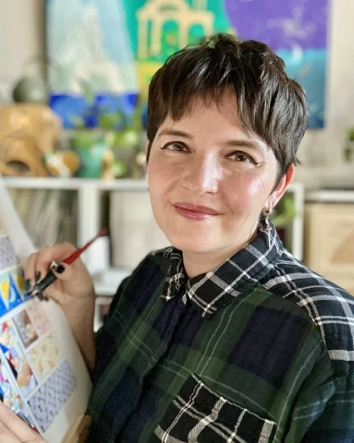 Woman with short dark hair smiling while working on an art project in a colorful studio.