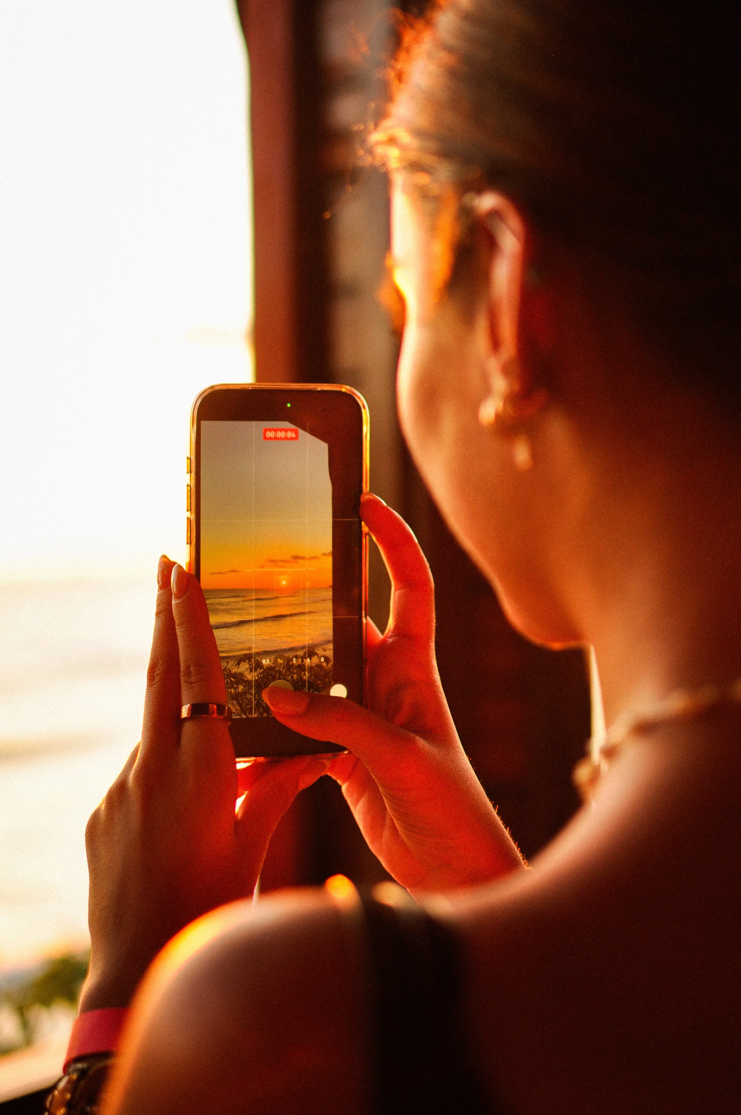 Person holding a smartphone capturing a sunset at the beach.