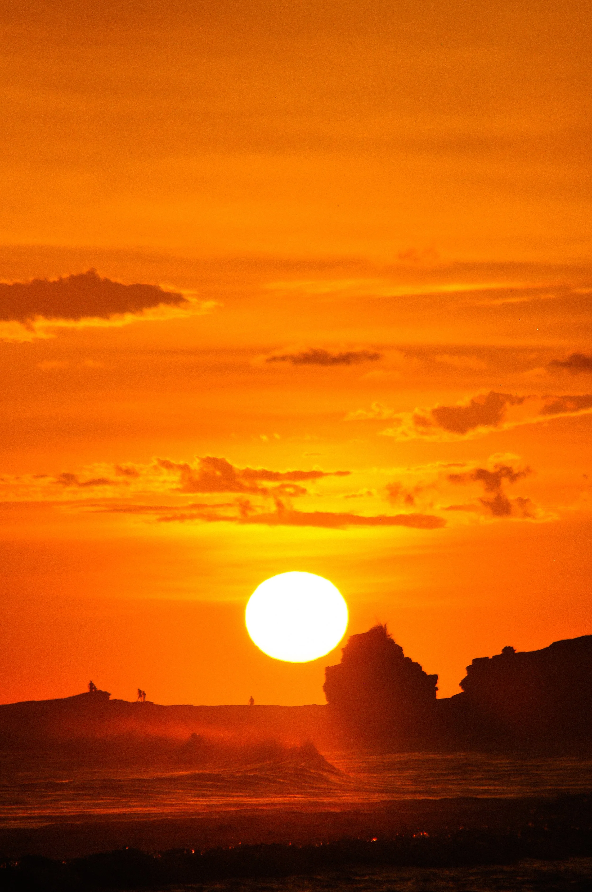 Sunset over ocean with silhouettes of cliffs and small figures in the foreground