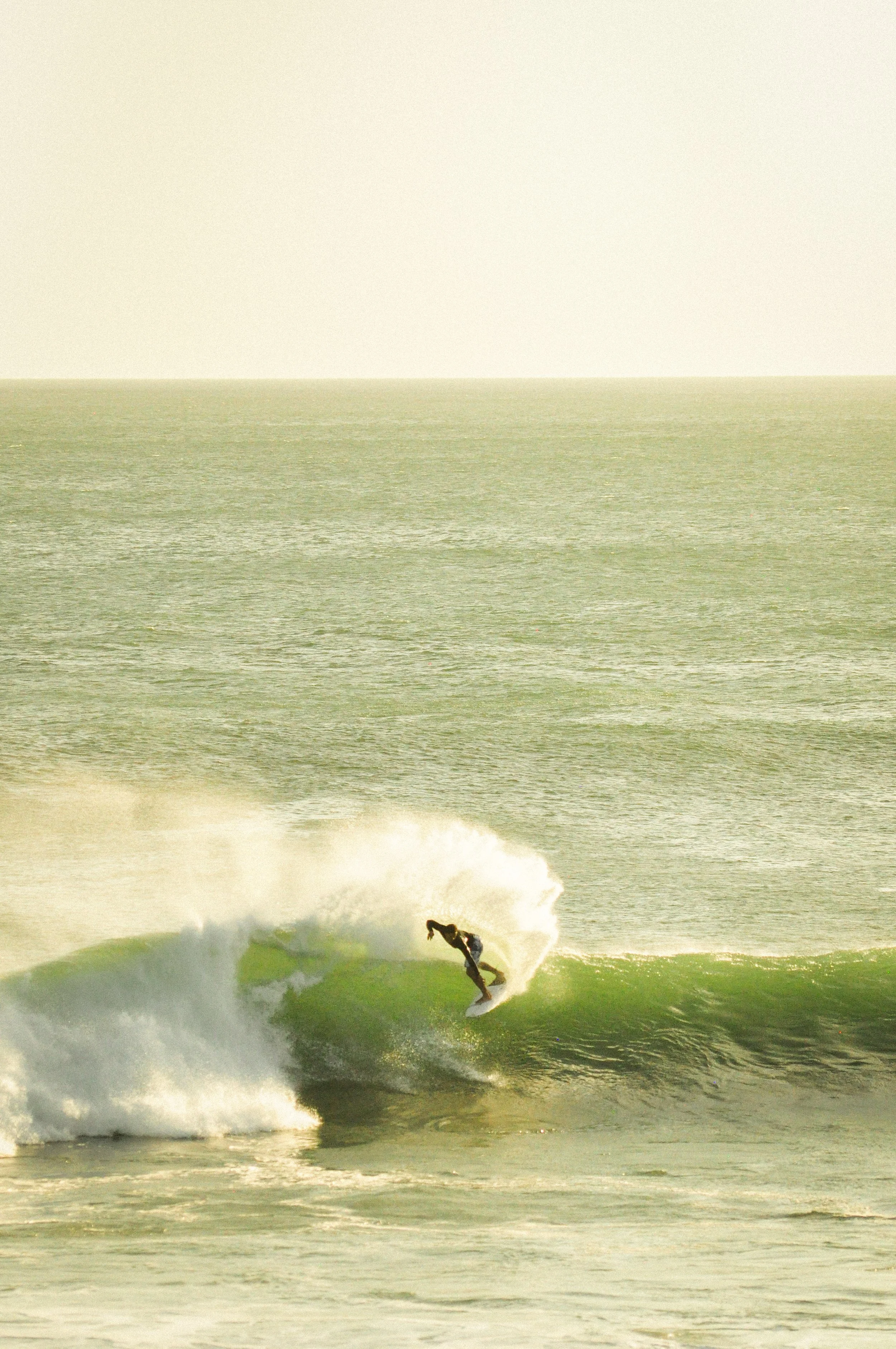A surfer riding a wave near the shore with a background of calm ocean and a cloudy sky.