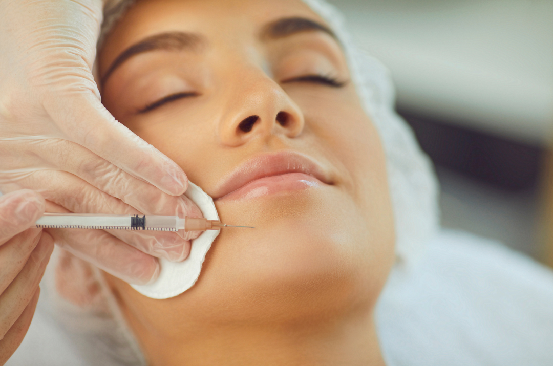 A woman receiving a cosmetic facial treatment with a syringe, her face relaxed and eyes closed.