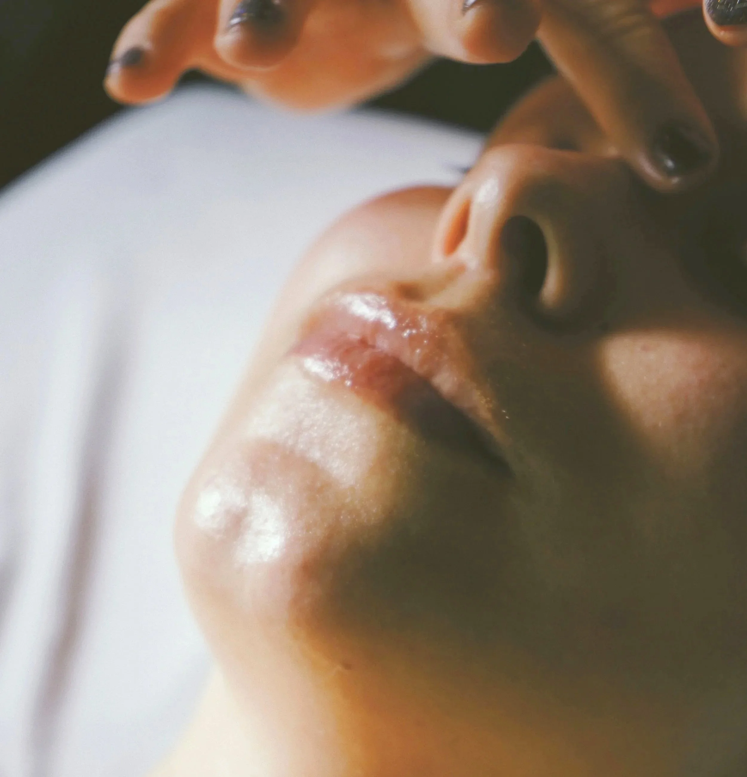 Close-up of a person's face with sunglasses and/or makeup, reflected in a mirror or surface, capturing a portion of their cheek and lips, with a deep-focus, artistic shot.
