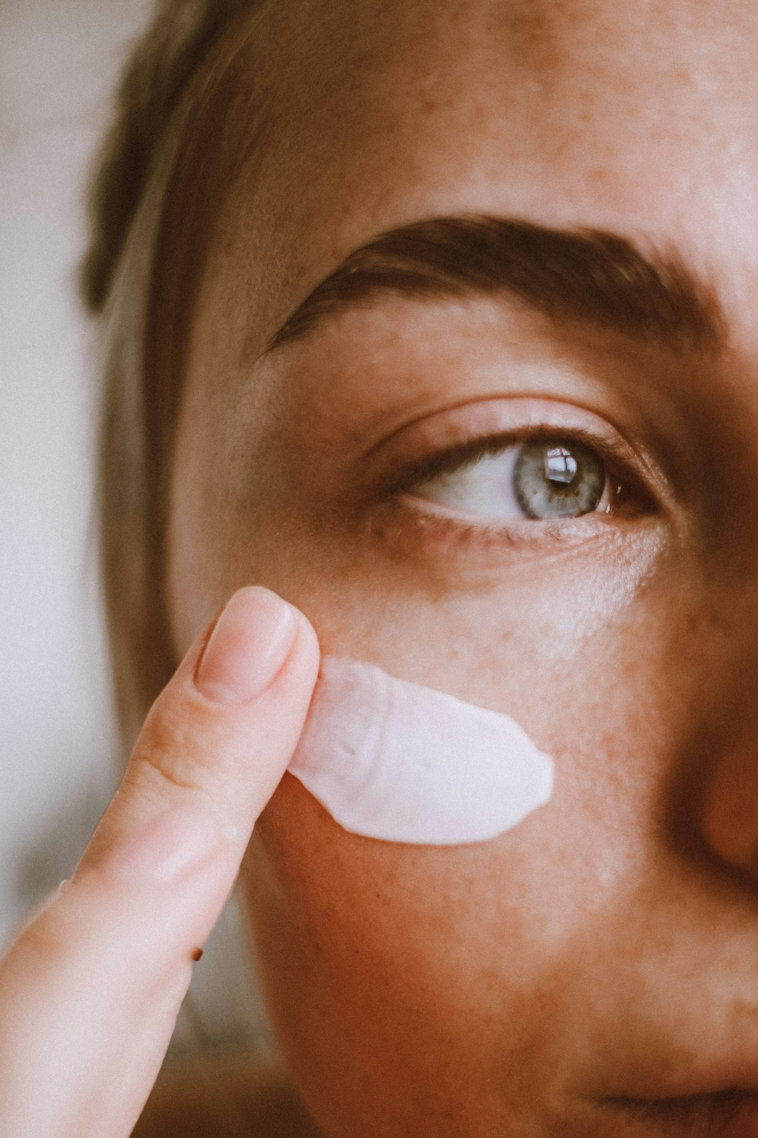 A person applying a white lotion or ointment under their eye area.