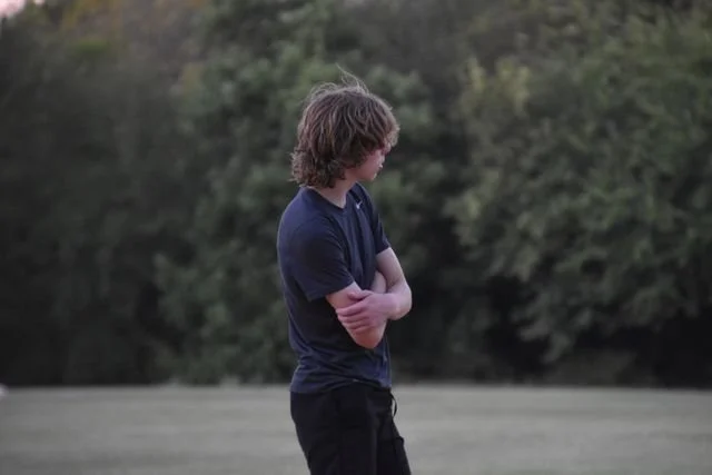 a teen boy standing alone with his arms crossed