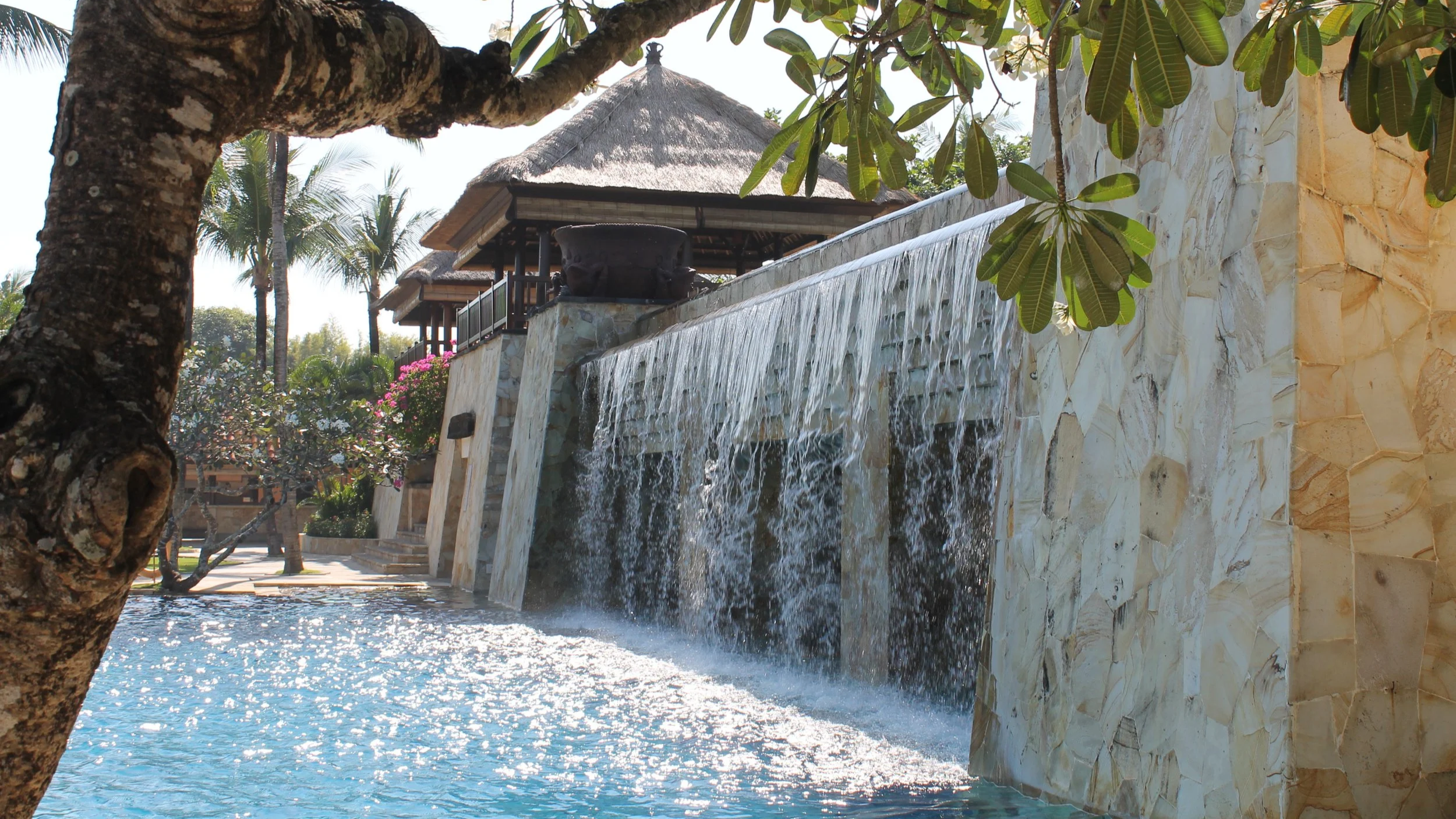 Pool waterfall surrounded by tropical gardens at AYANA Resort Bali, Indonesia