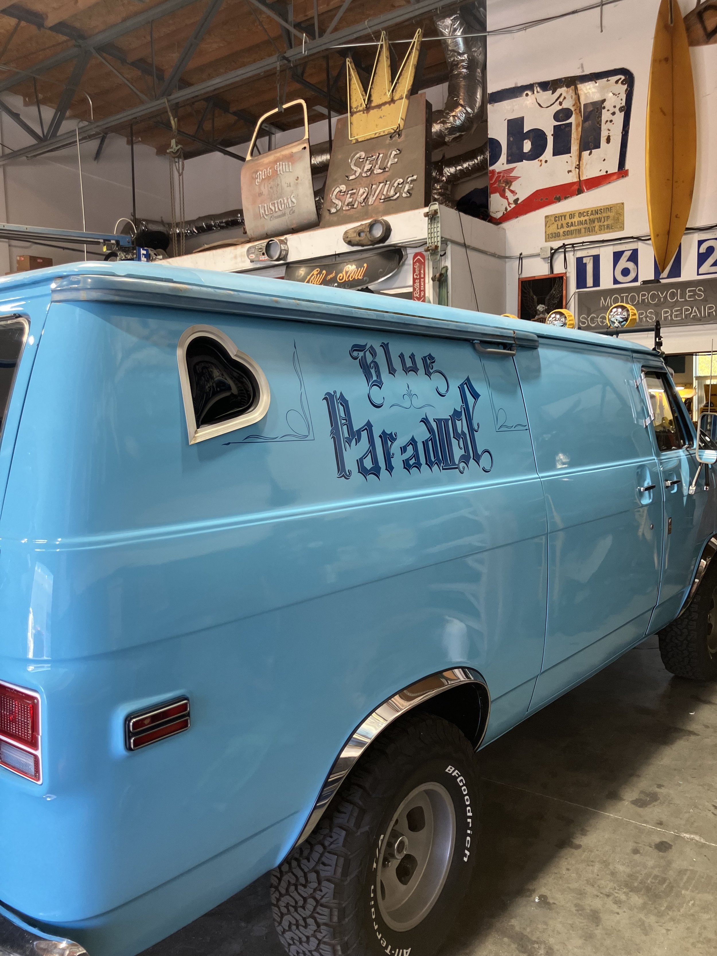 A blue van with custom lettering on the side, parked indoors among vintage signs and memorabilia.