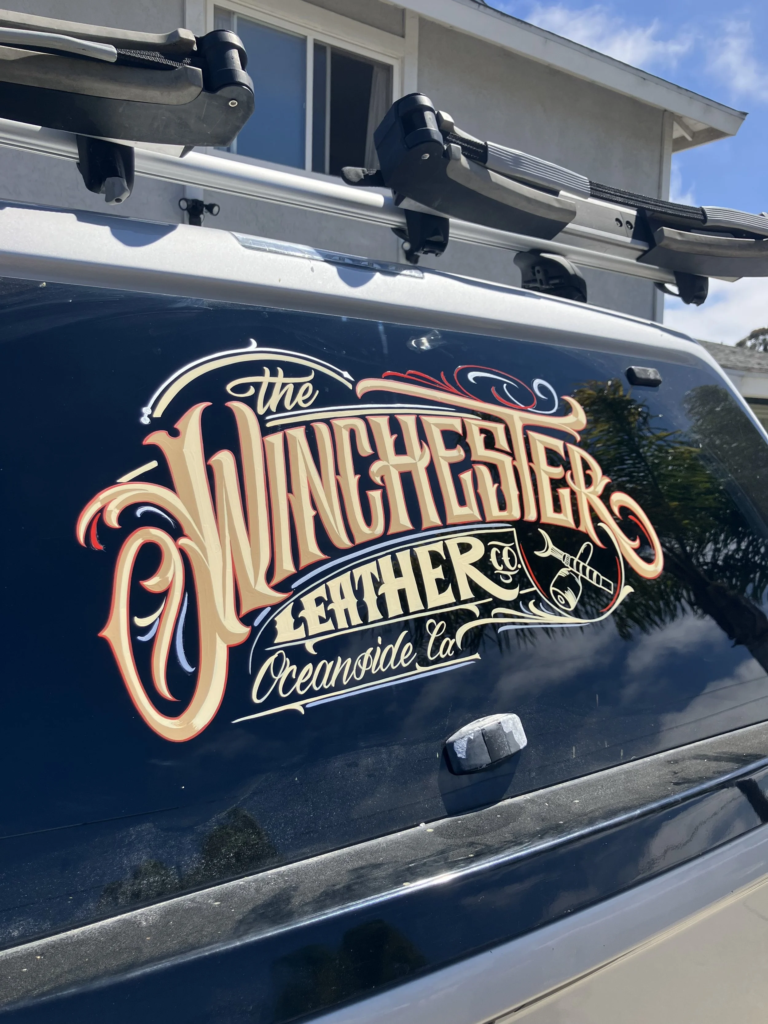 A vehicle with a decorative decal on its rear window reading "the Wunchers" with additional text indicating it is from Oceanside, California, along with graphic elements such as a drum and drumsticks. The image also features part of a roof rack on to