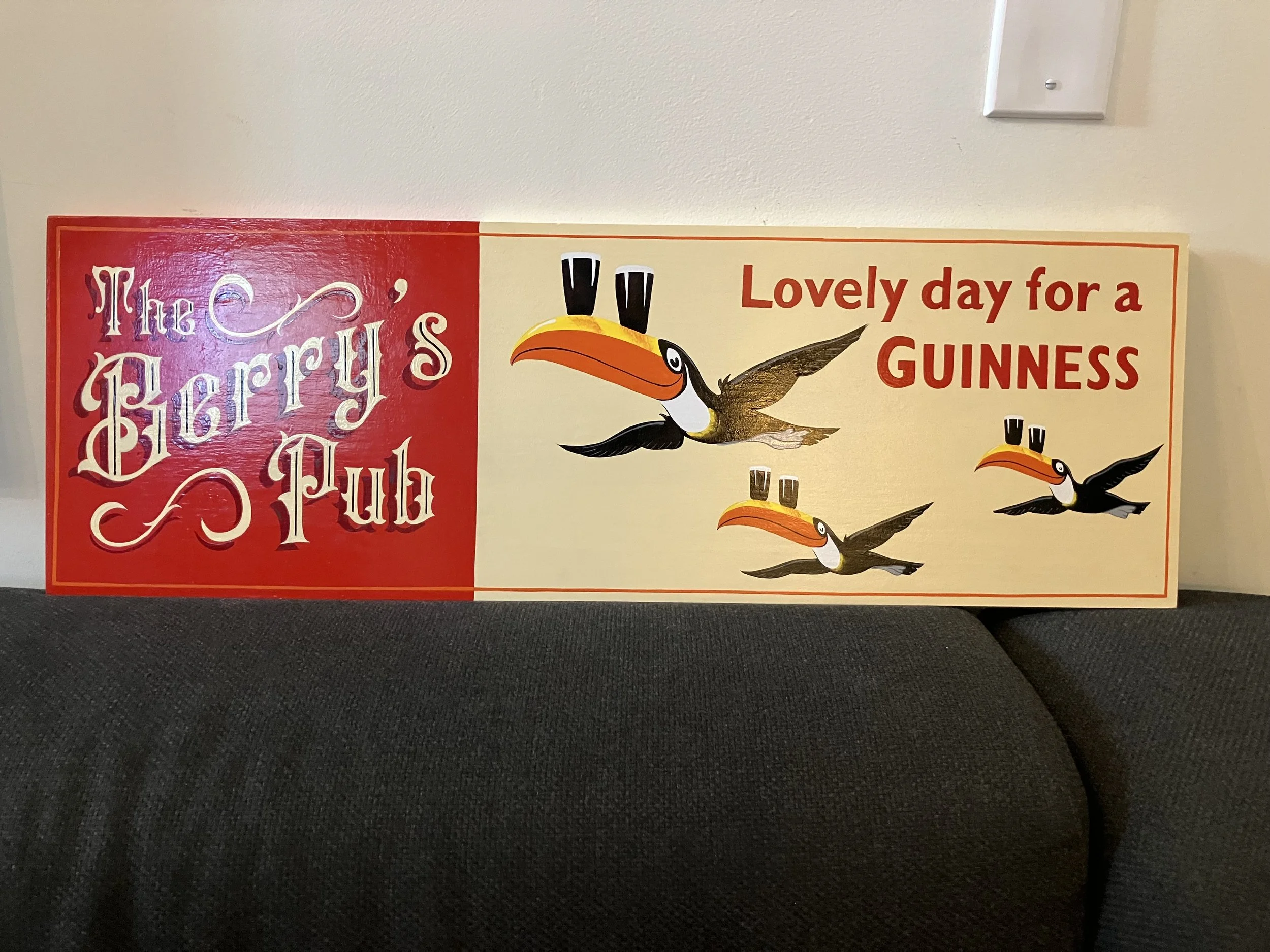 A carnival-style poster with a red and white color scheme, featuring a cartoon toucan with a large, orange beak and black wings, accompanied by the phrase "Lovely day for a GUINNESS". The poster also includes decorative text on the left side, possibl
