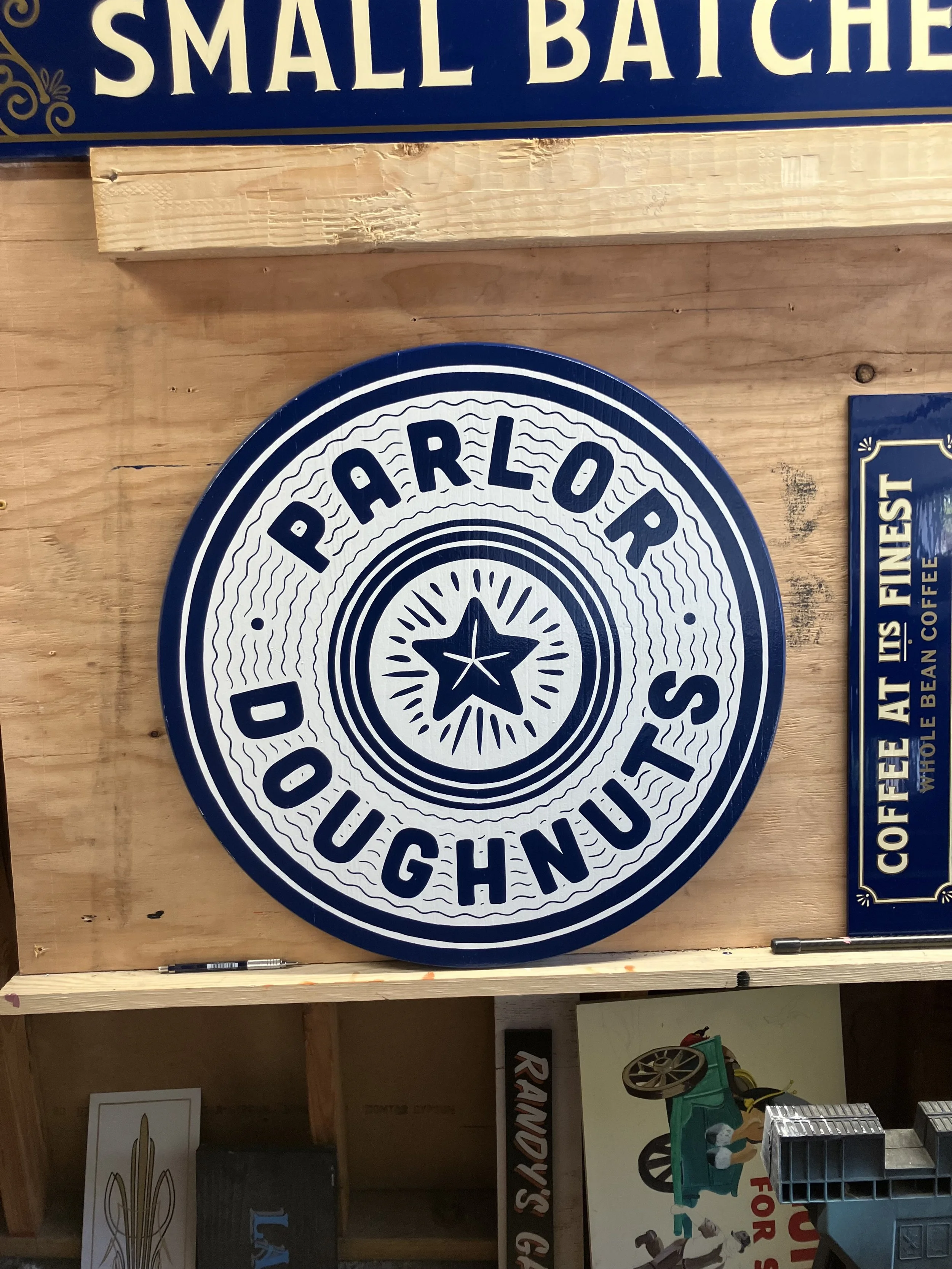 A circular sign with the text "PARDON DON" in a ring around a star motif at the center, mounted on a wooden wall.
