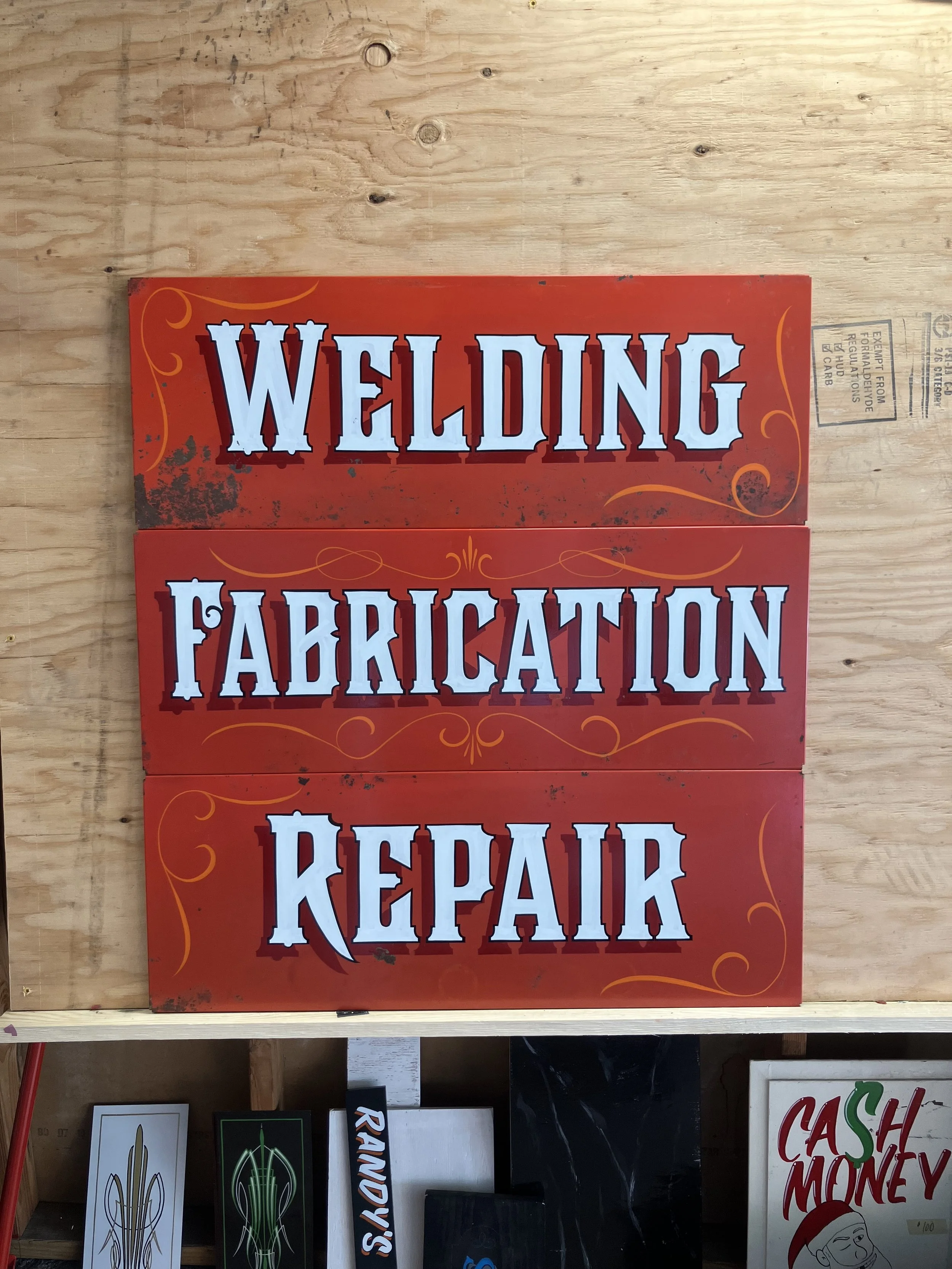 Sign with the words 'WELDING,' 'FABRICATION,' and 'REPAIR' in large, stylized letters on a red background with decorative swirls.