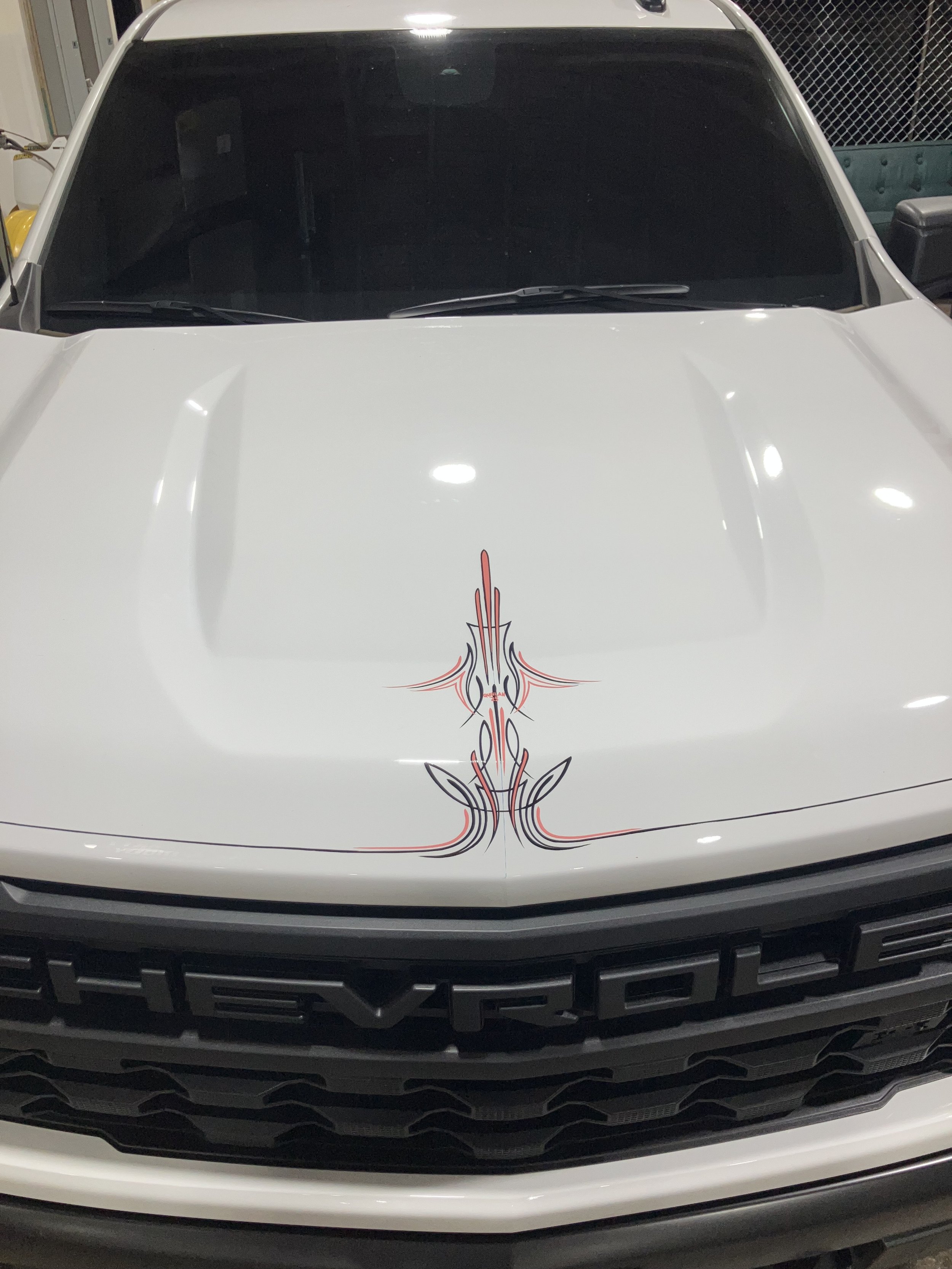 Front view of a white vehicle with a tattoo-style decal design on the hood and a black grille.