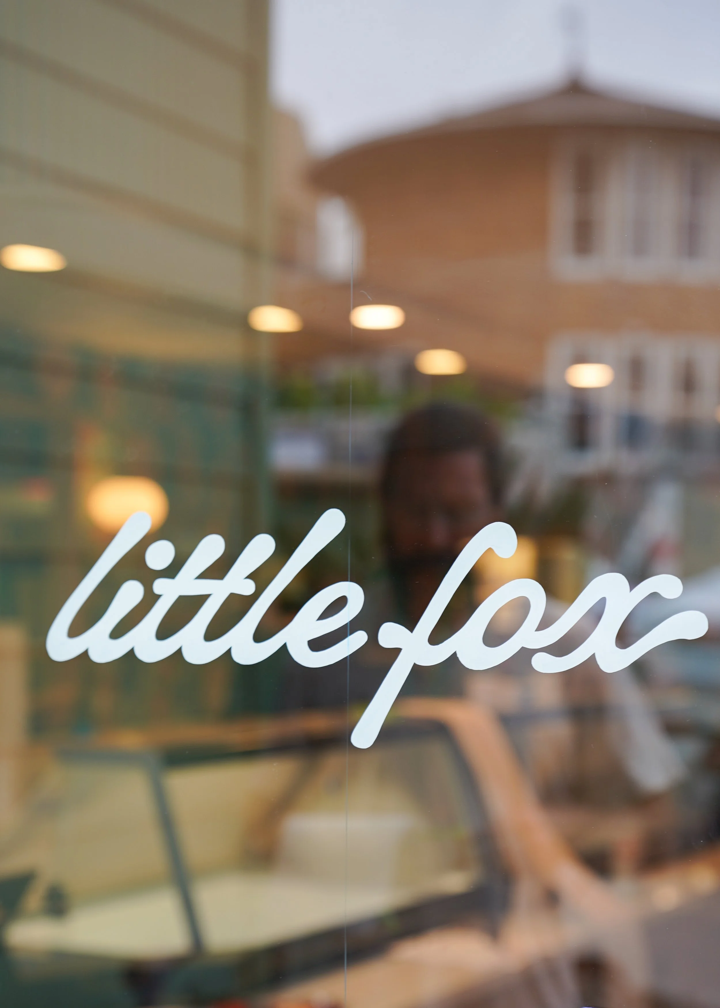 Close-up of a window sign with the words 'little shop' written in white cursive font.