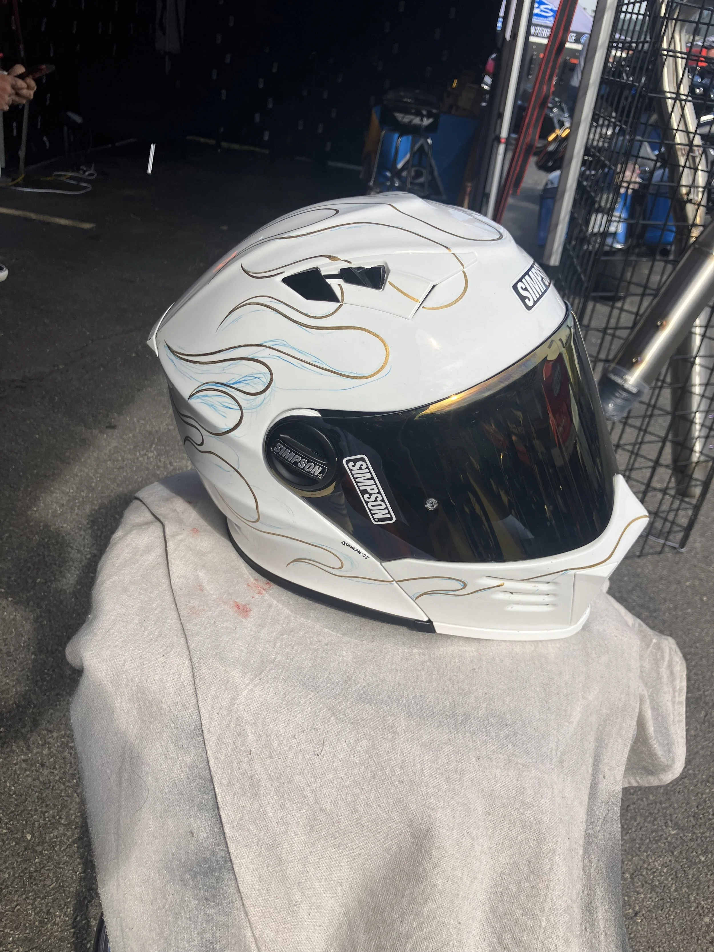 A motorcycle helmet with white and black design and decorative flames in black and blue on the sides, resting on a cloth on a surface.