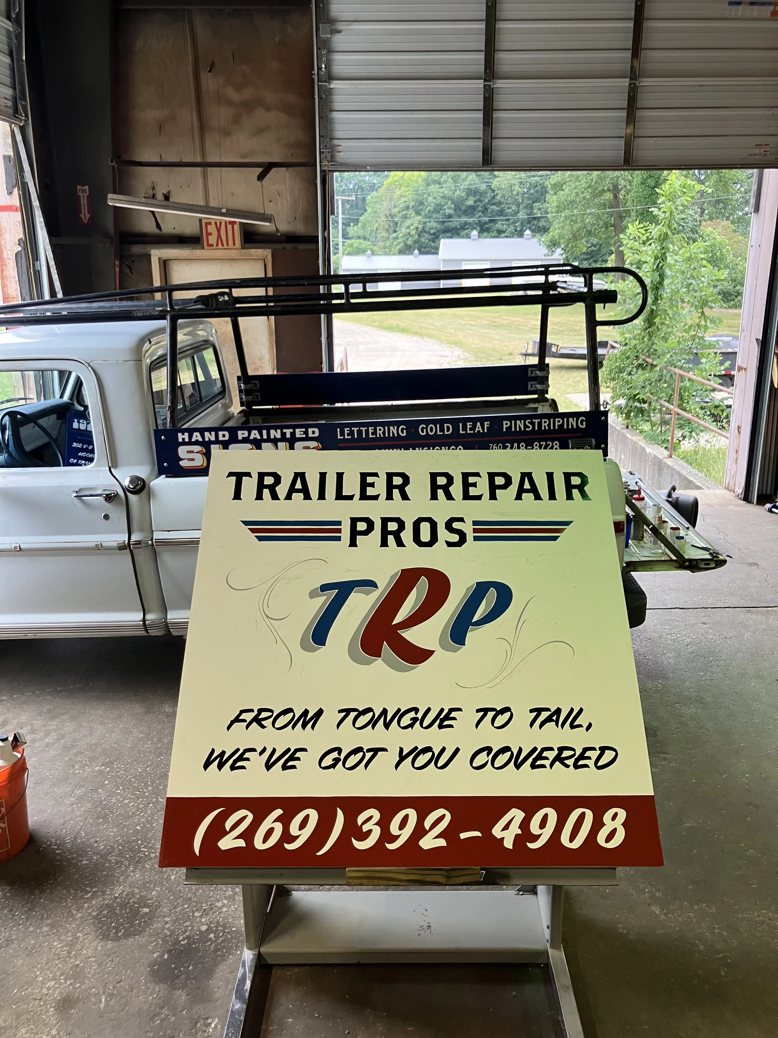 Sign advertising trailer repair services with the text: 'TRAILER REPAIR PROS from tongue to tail, we've got you covered' and a phone number.