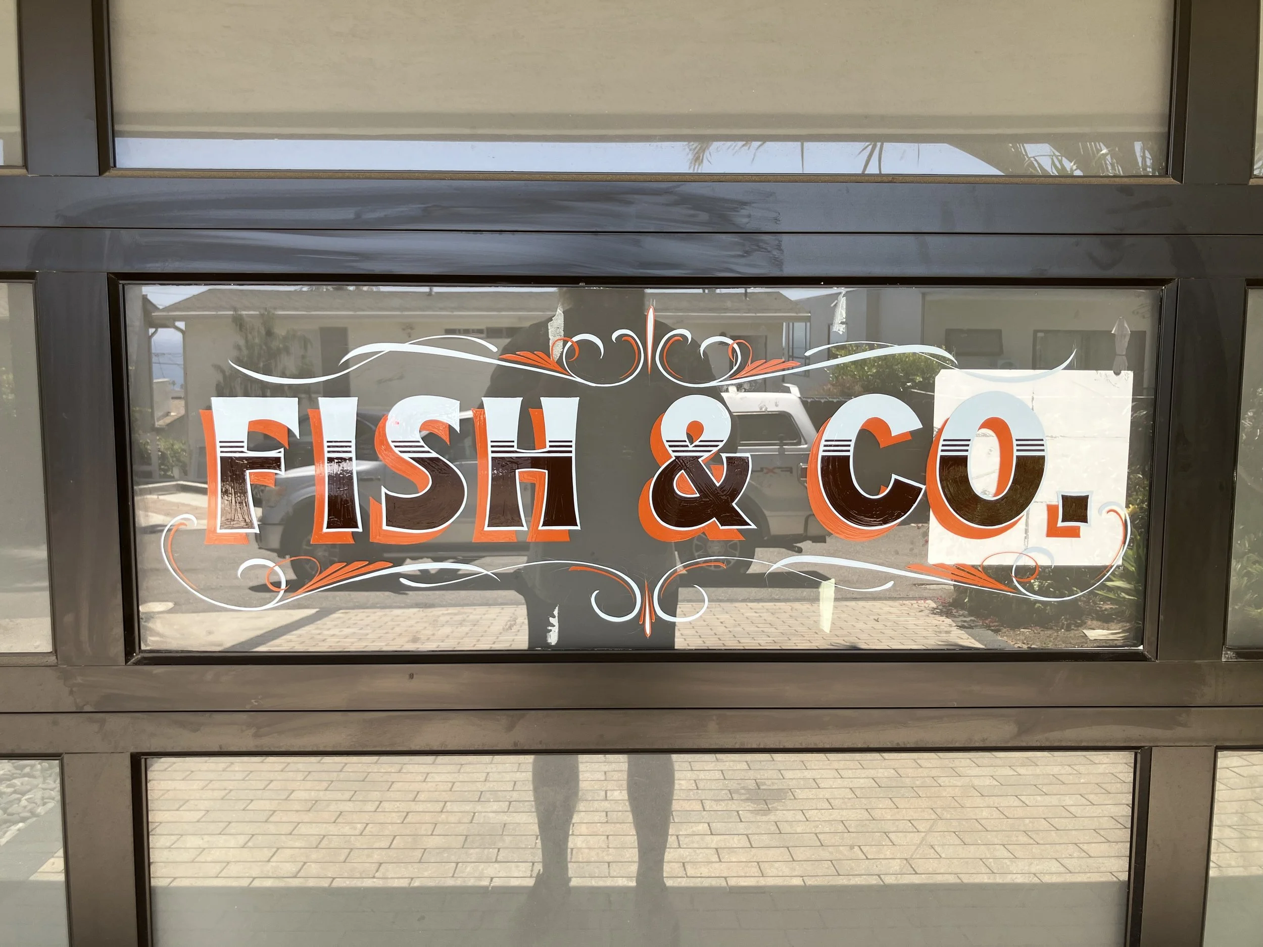 Decorative sign on glass door with the words "FISH & CO" in large, bold, orange and white letters, with white and orange decorative flourishes above and below.