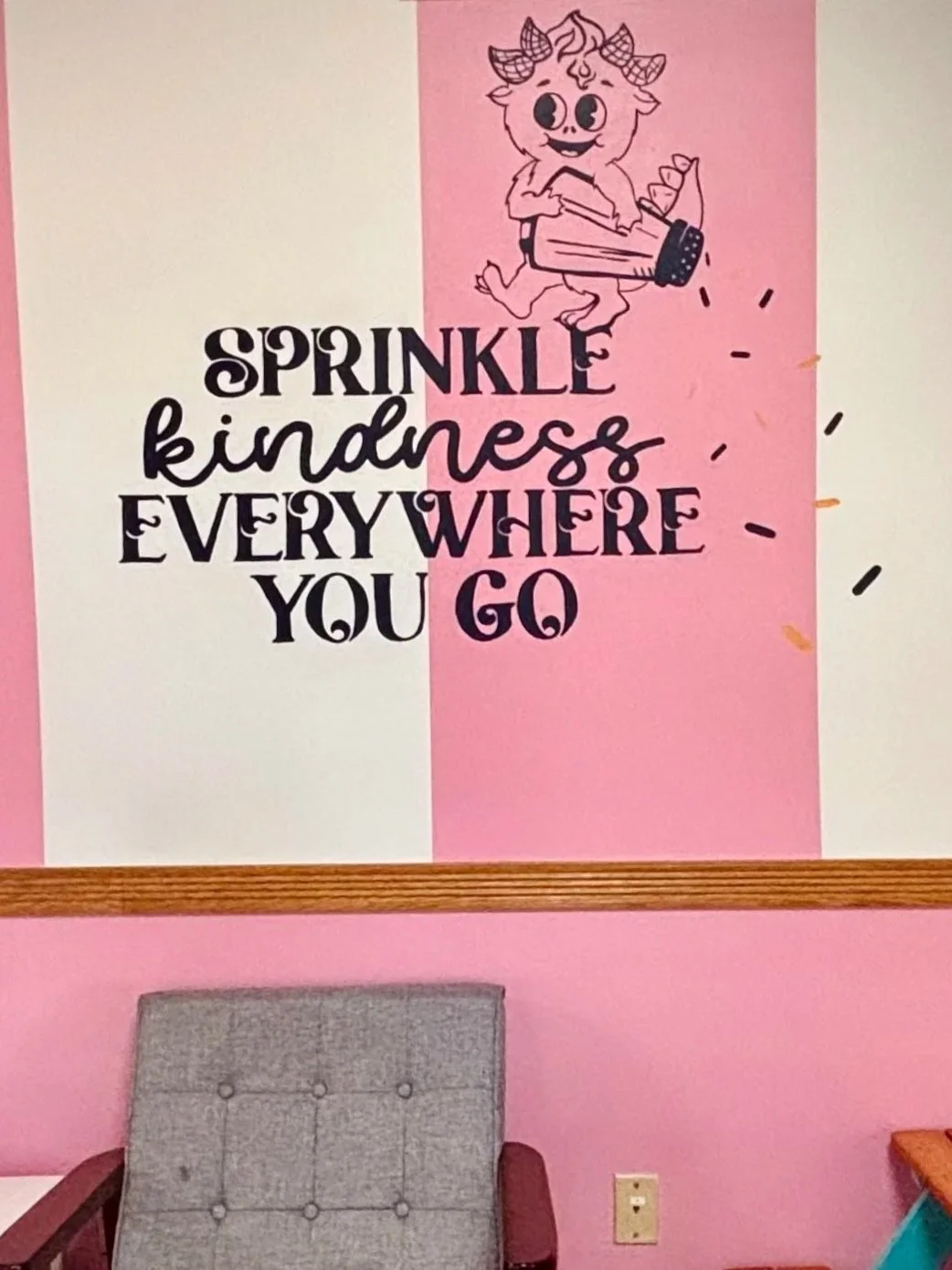 Pink and white wall with a cartoon monster holding a sprinkle shaker, along with the quote "Sprinkle kindness everywhere you go" in decorative blue text.